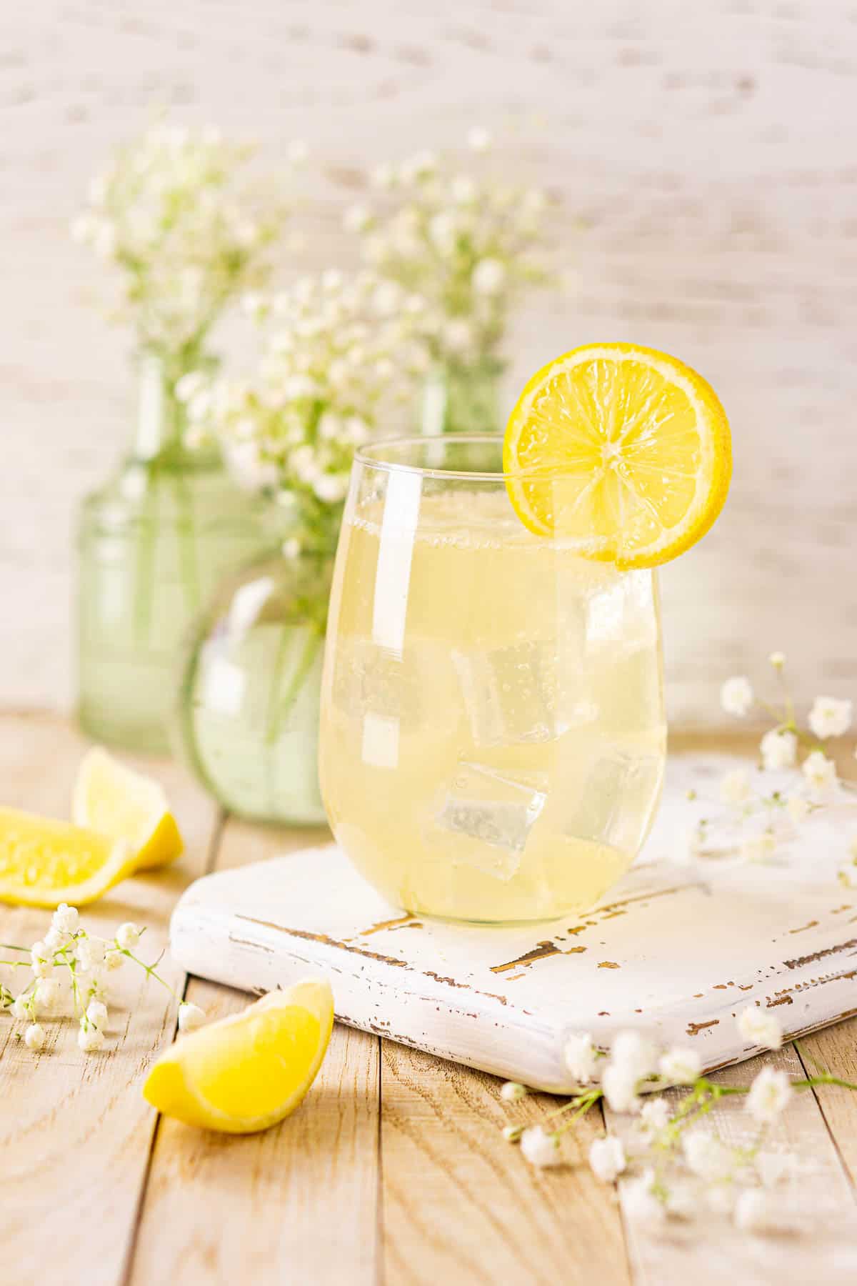 A straight-on view of the St. Germain elderflower spritz on a white wooden tray with white flowers in the background and lemon slices to the side.