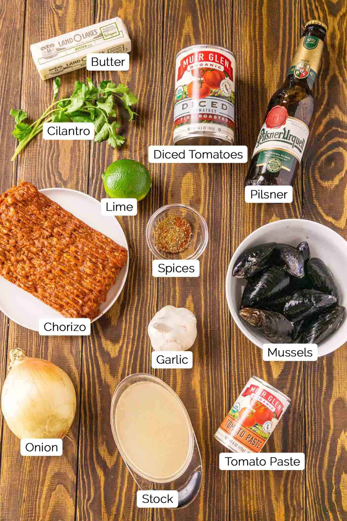 The ingredients for the beer mussels on a brown wooden board with black and white labels by each item.
