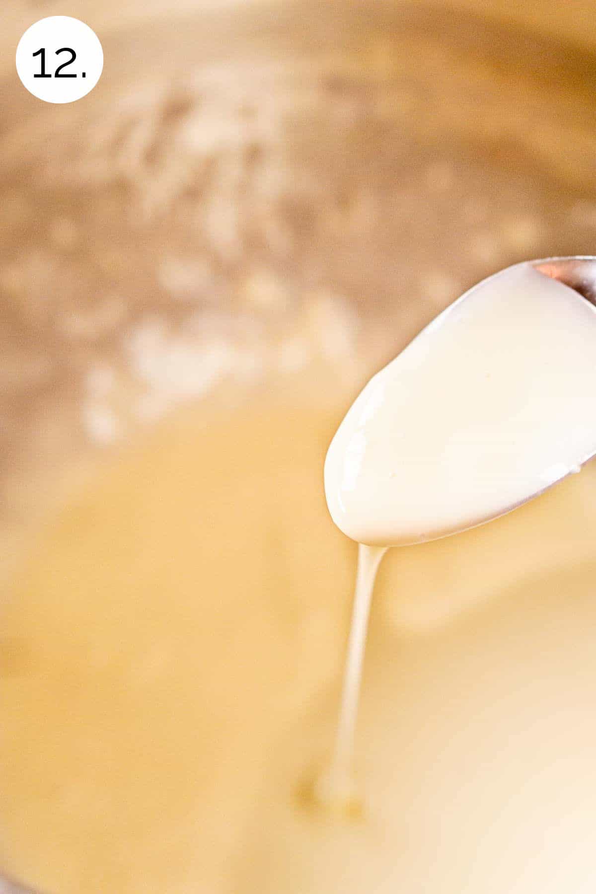 A spoon drizzling the cream cheese glaze into a large stainless steel mixing bowl to show the consistency.