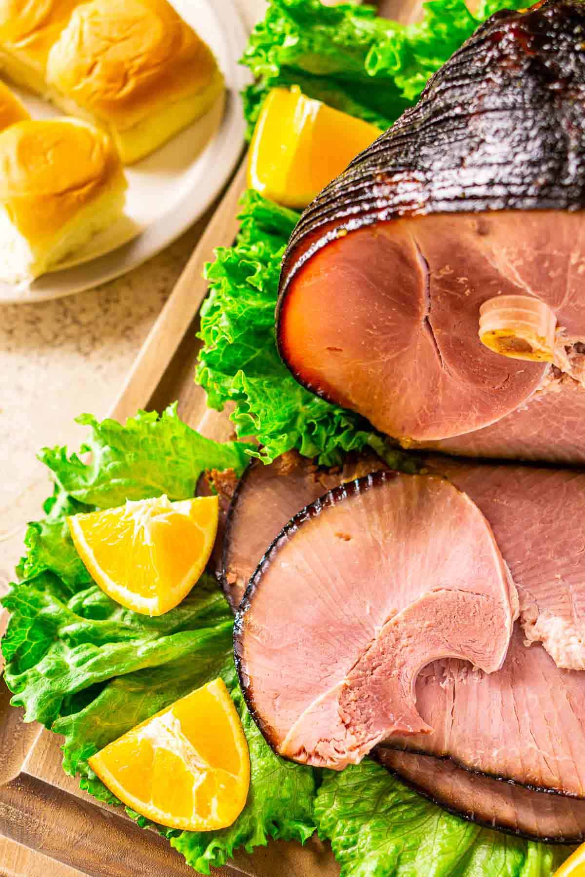An aerial view of the double-smoked ham on green lettuce and a cutting board with a plate of rolls in the corner.