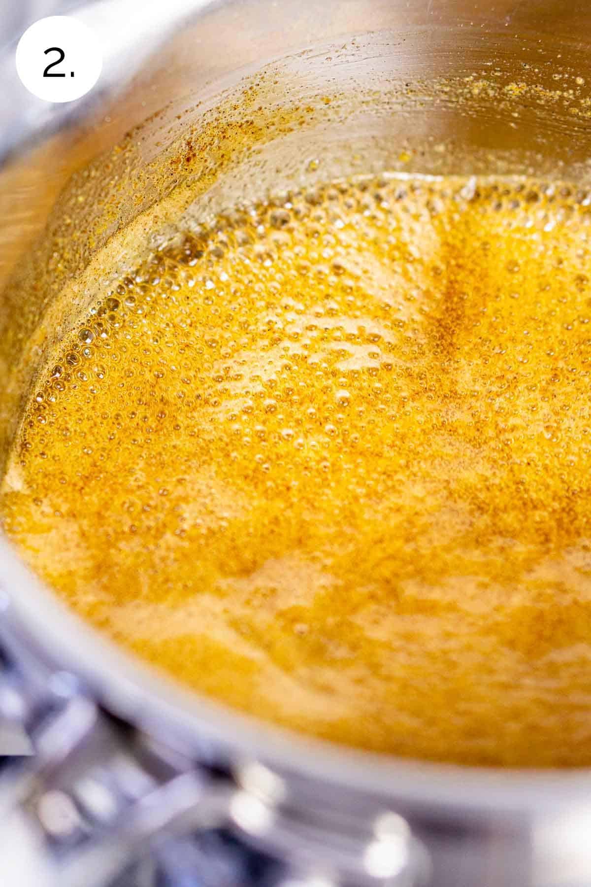 The spiced orange glaze boiling in a small stainless steel saucepan on the stove-top range.