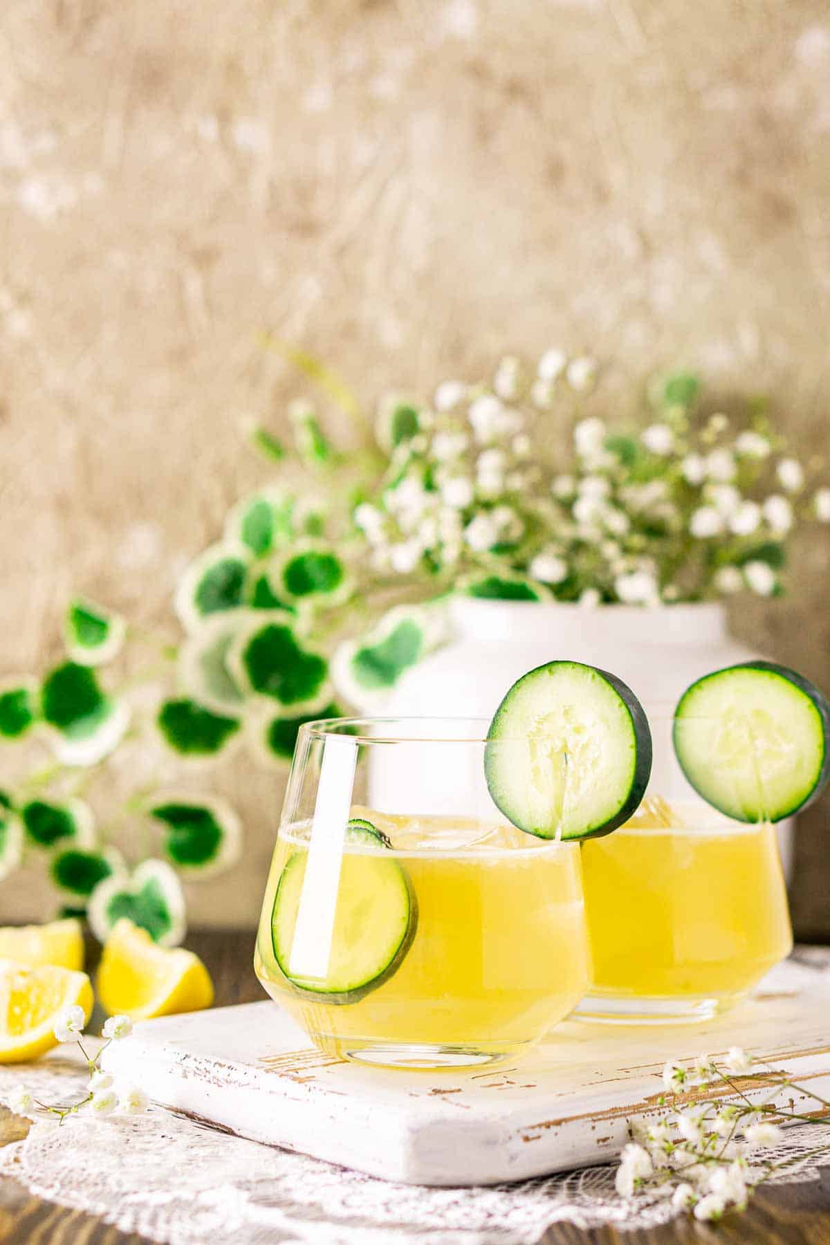 A close-up shot of the Irish Maid cocktail on a white tray with a green planter in the background and flowers and lemons to the side.