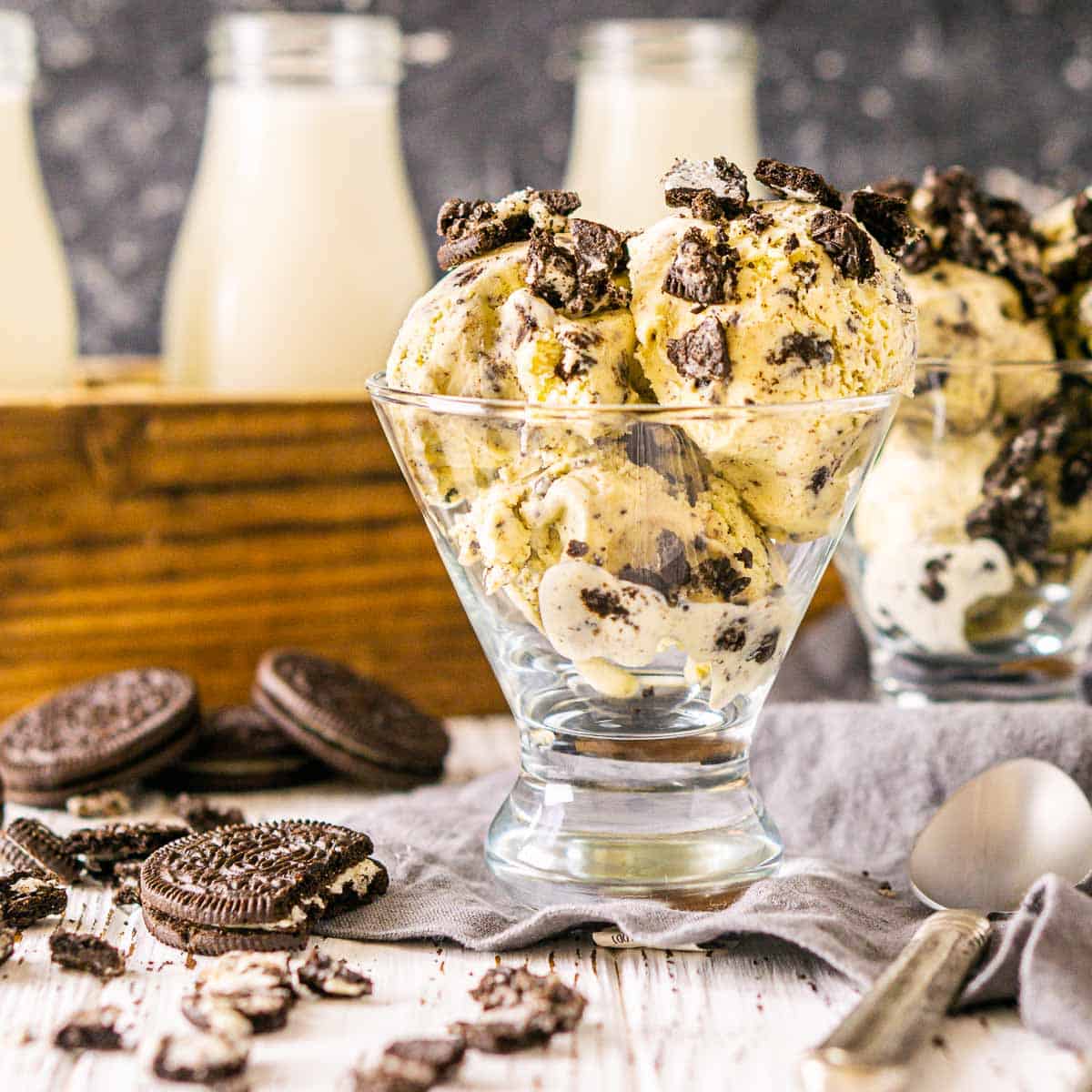 A cup of Oreo ice cream with spoons to the side on a white surface.