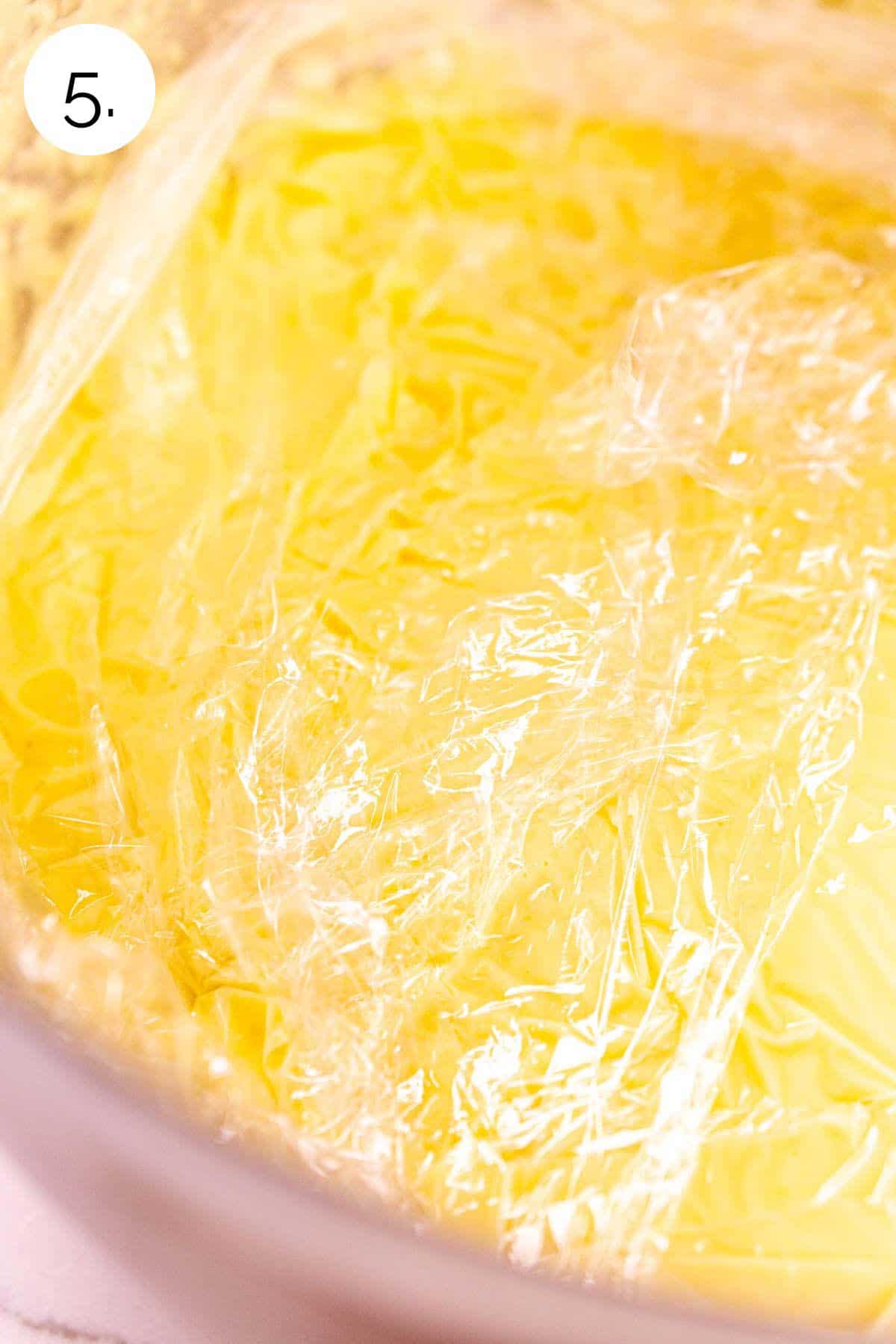 The custard mixture in a large bowl with plastic wrap placed directly on the surface to keep a film from forming.