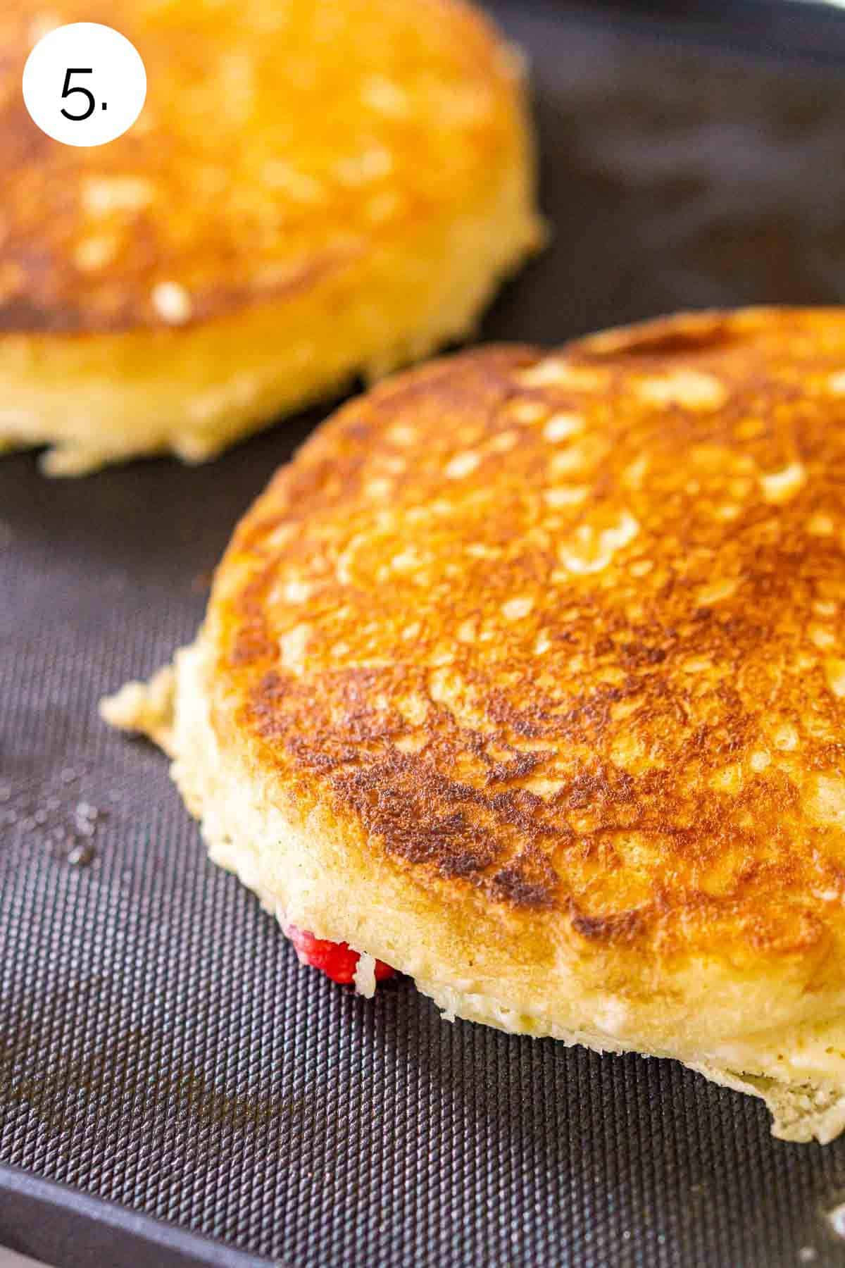 The pancakes cooking on the second side of an electric griddle after the first side turned golden brown.