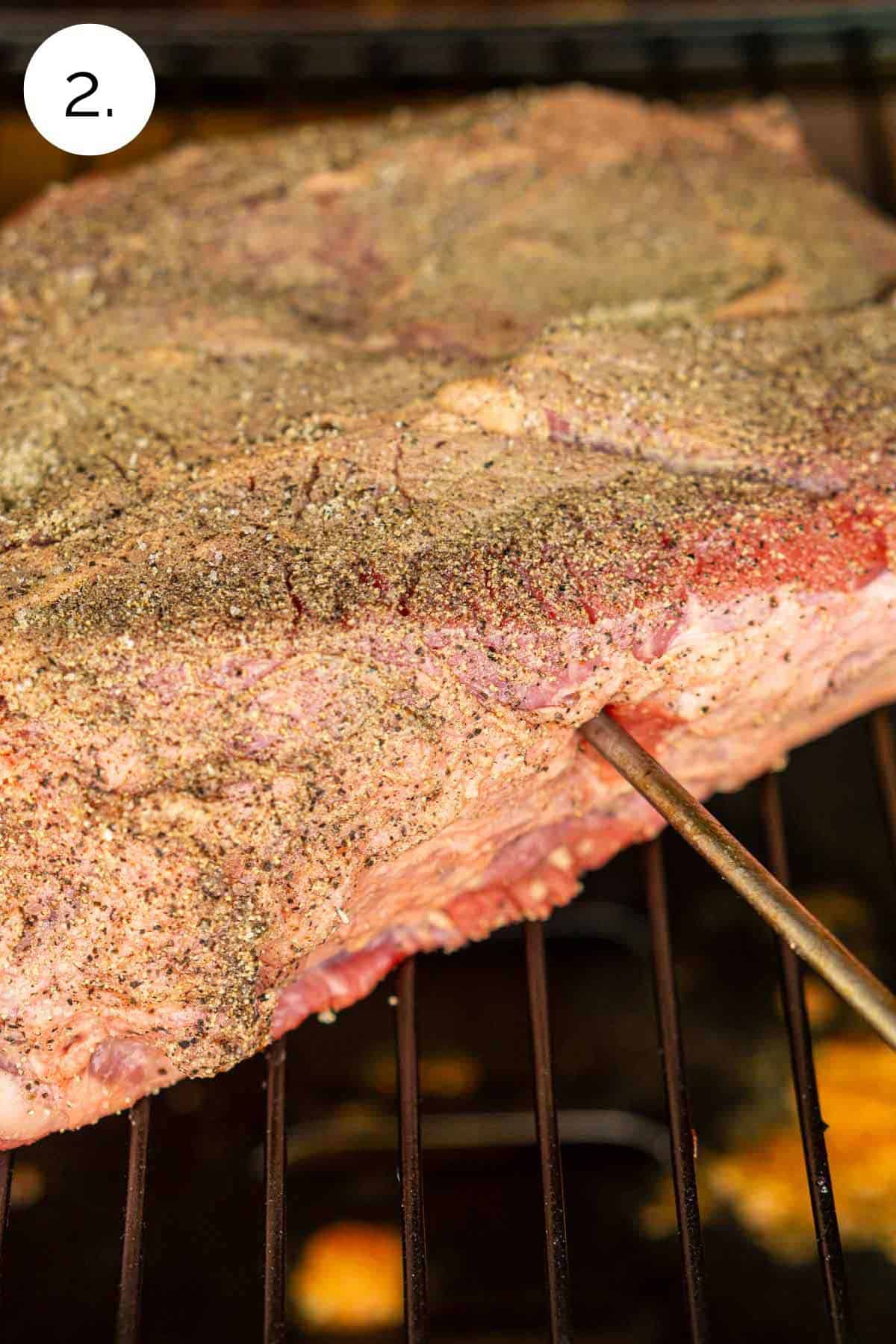 The chuck roast on the grill grates of the smoker with a leave-in meat thermometer inserted in the center of the meat.