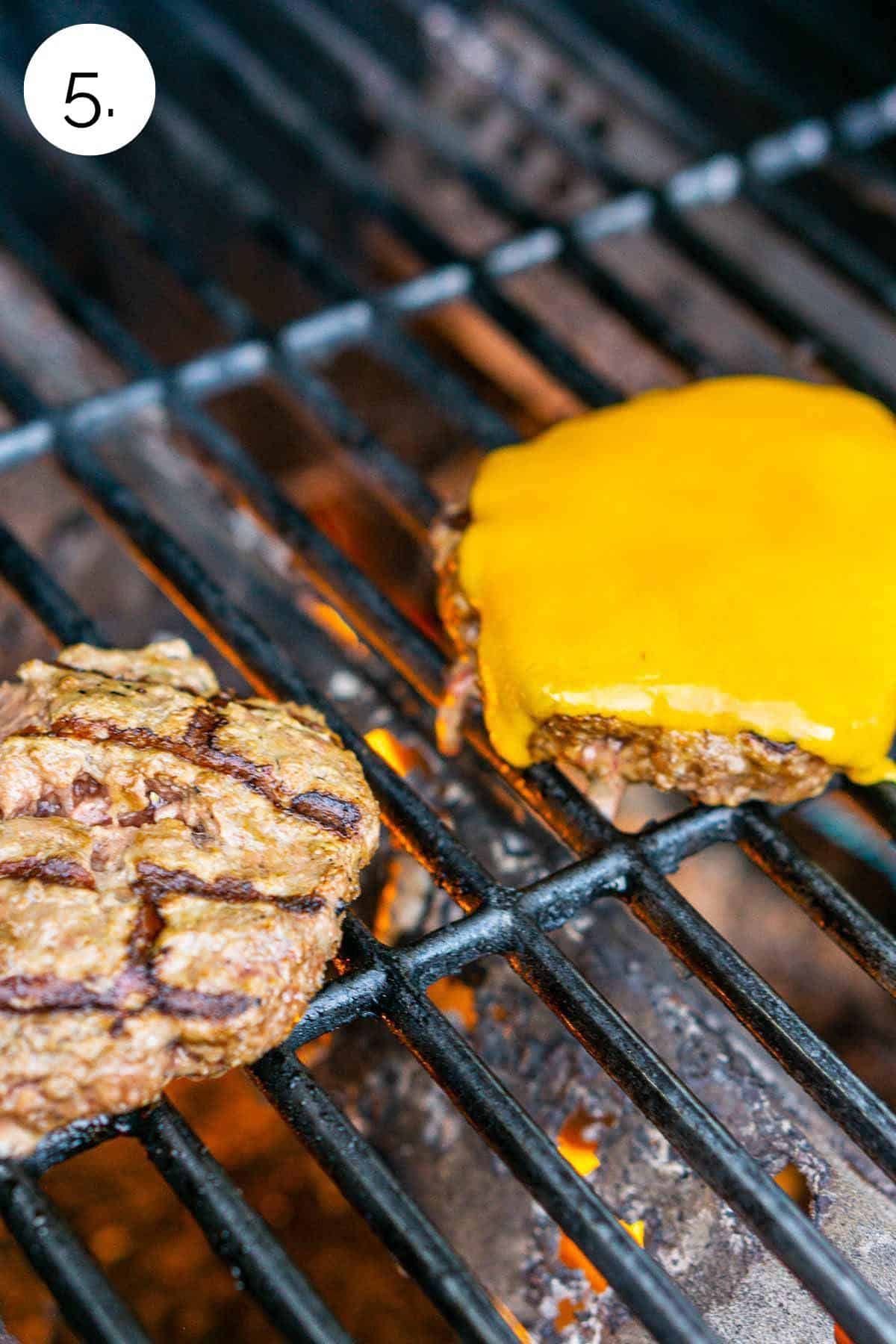 The burgers on the grill with a slice of cheddar cheese on top of one patty.