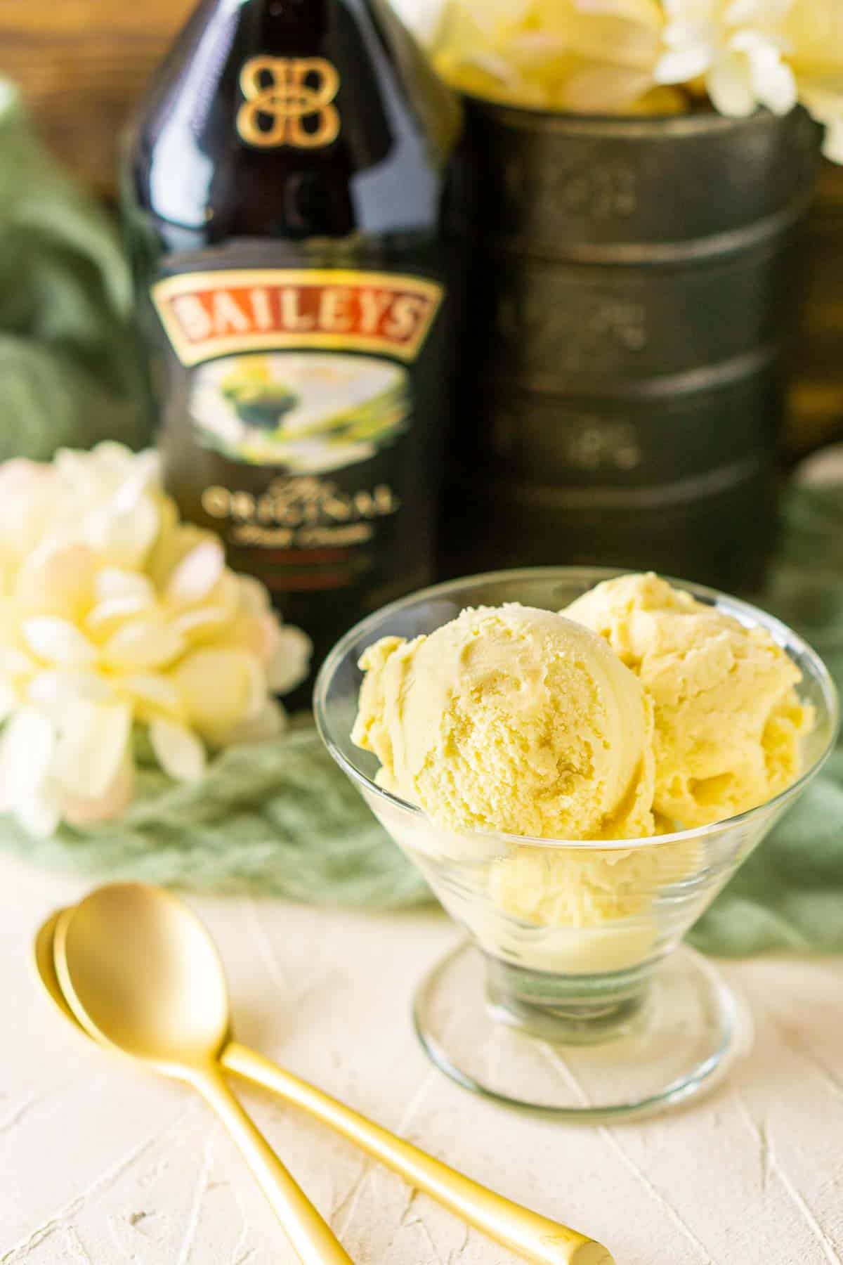 Two gold spoons stacked on top of each other next to a glass cup of Baileys ice cream.