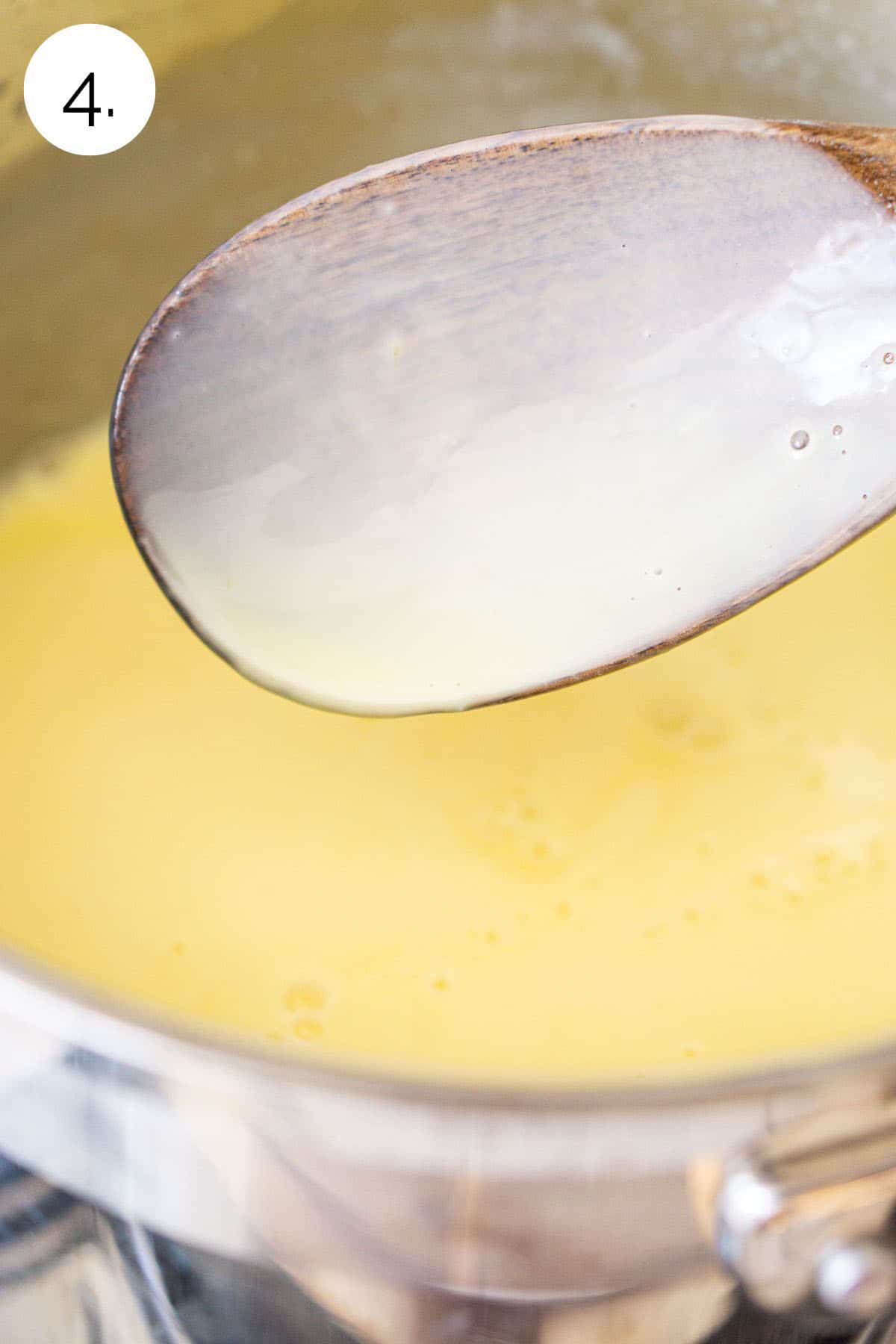 A wooden spoon over a small stainless steel saucepan with the custard base covering it.