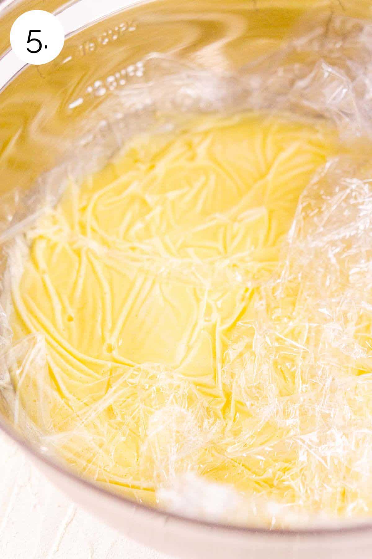 The ice cream base in a large mixing bowl with plastic wrap directly on the surface of the custard before refrigerating.