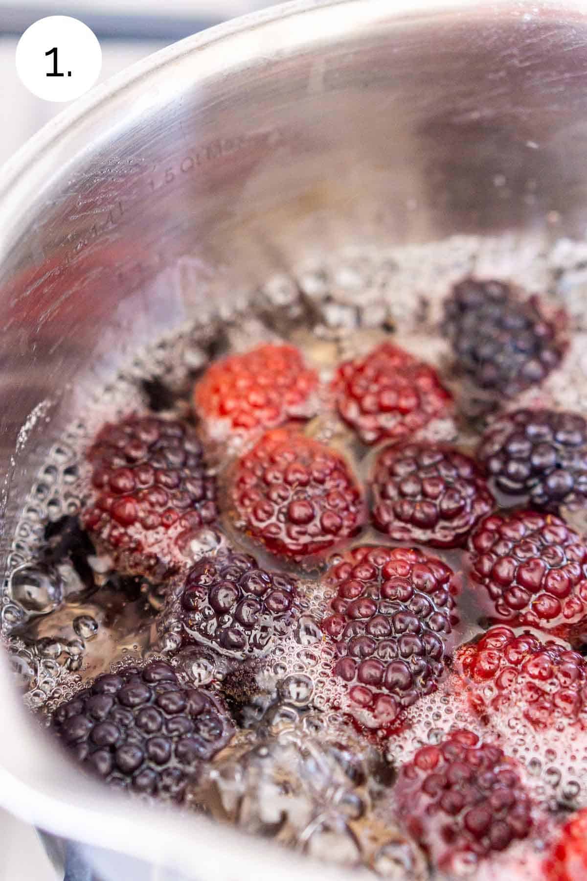 The blackberries, water and sugar boiling in a small stainless steel saucepan on the stove.