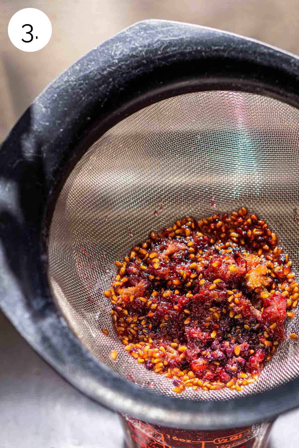 Straining the crushed blackberries from the syrup in a fine-mesh sieve over a kitchen sink.