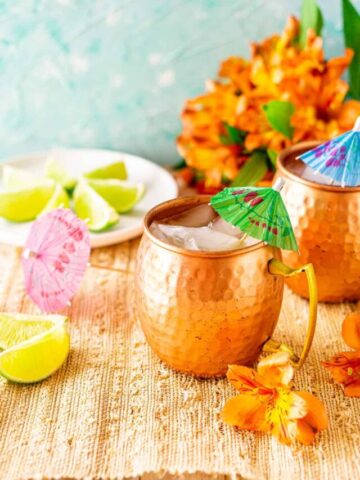 Looking down on a Jamaican mule on a straw placemat with lime slices and tropical orange flowers to the side.