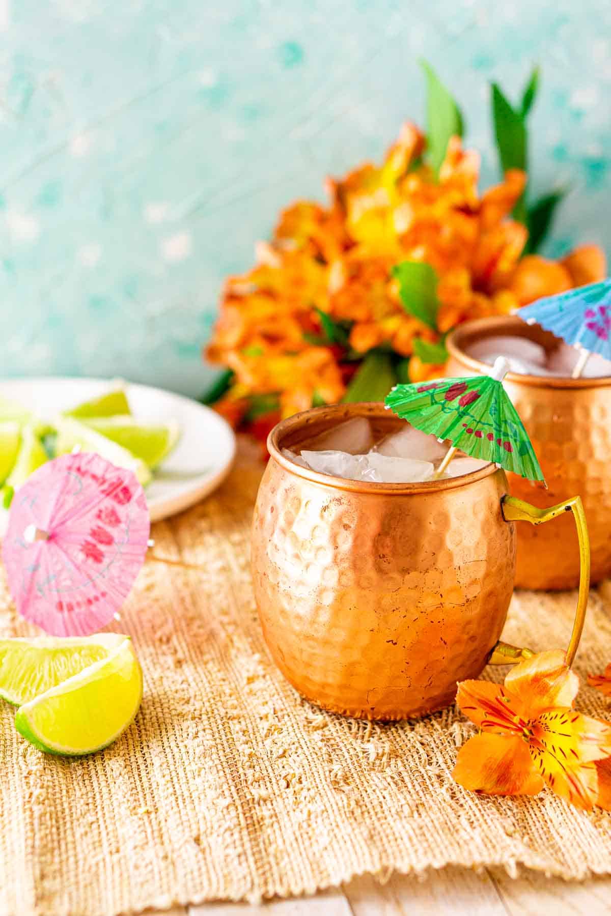 A side view of a Jamaican mule on a straw placemat with lime slices and orange flowers around it.