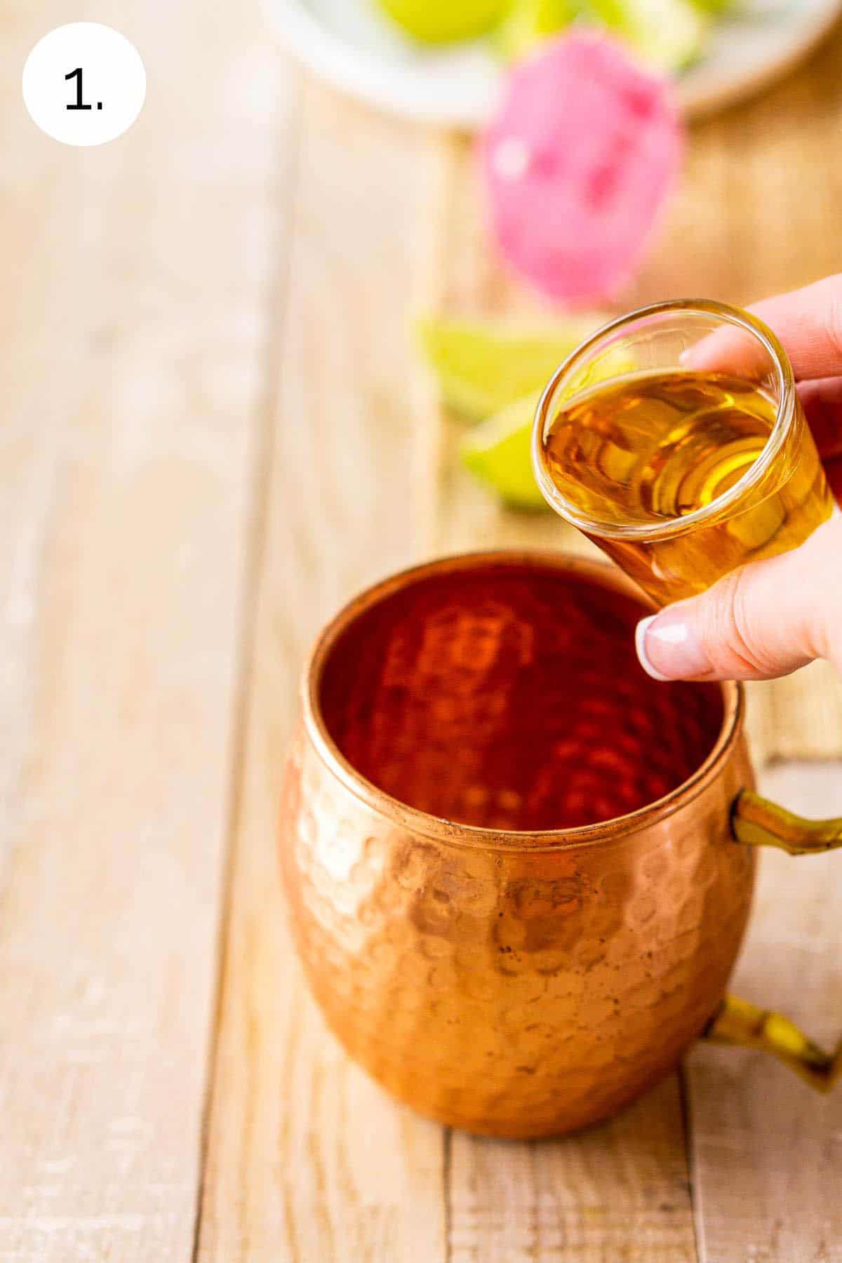 A hand pouring a shot of Jamaican rum into a copper mug on a cream-colored wooden board.