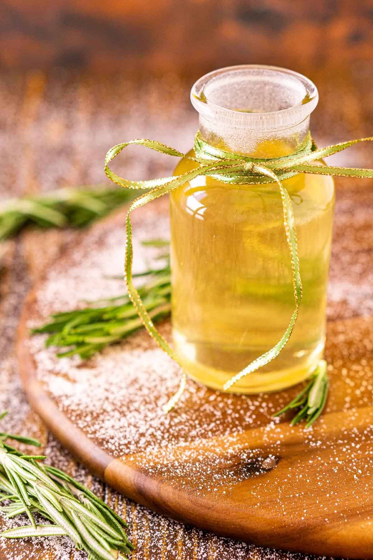 A bottle of the rosemary simple syrup against a wooden background on a serving tray with sugar sprinkled around it.