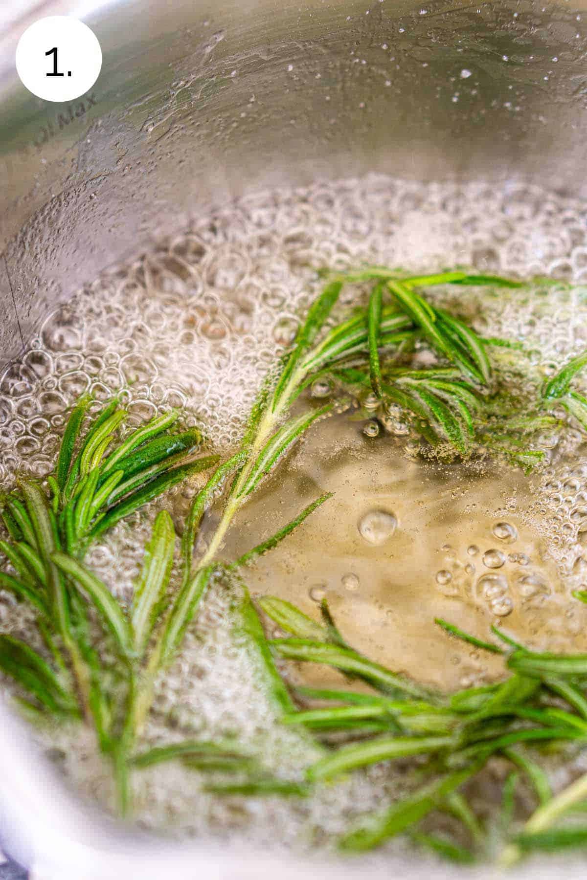 The water, sugar and rosemary boiling in a small stainless steel saucepan on the stove.
