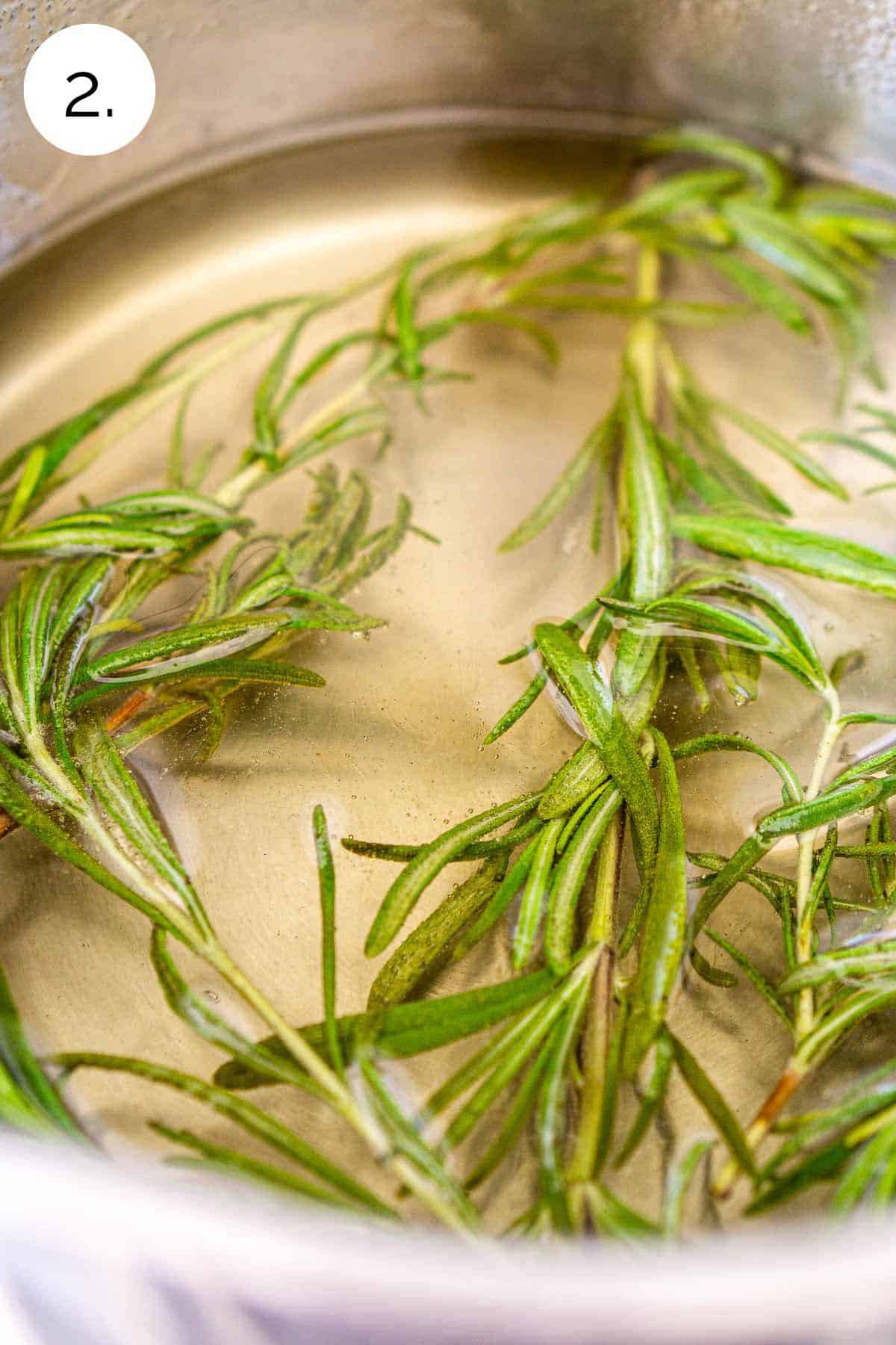 The rosemary sprigs steeping in the sugar syrup in a small stainless steel saucepan on the stove.