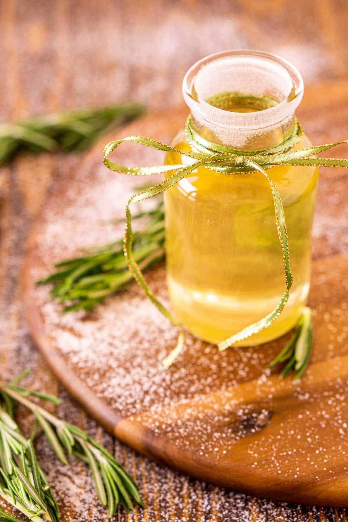 Looking down on a bottle of rosemary simple syrup on a wooden serving tray with sugar and fresh herbs around it.