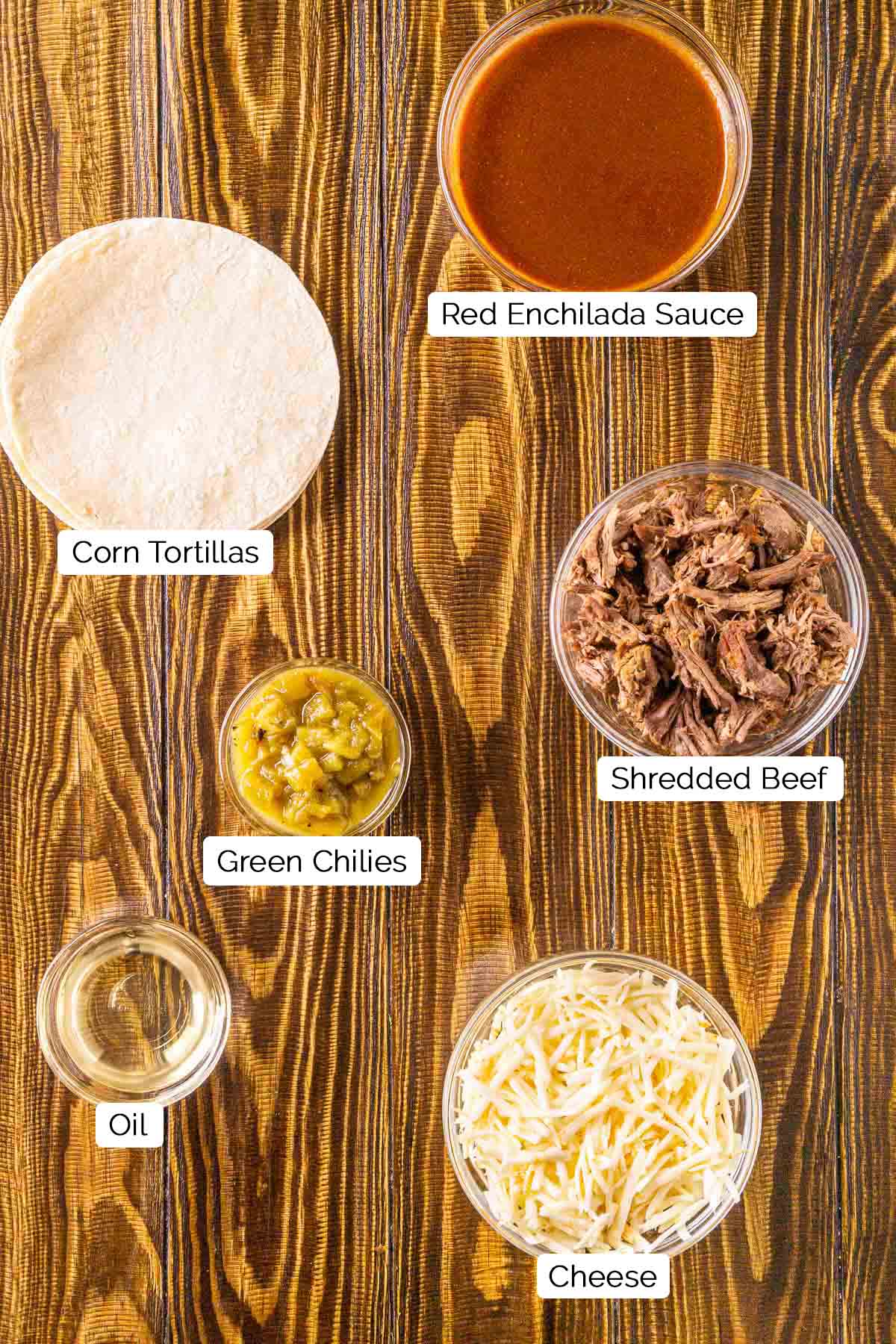 The ingredients for the beef enchiladas on a brown wooden board with black and white labels by the items.