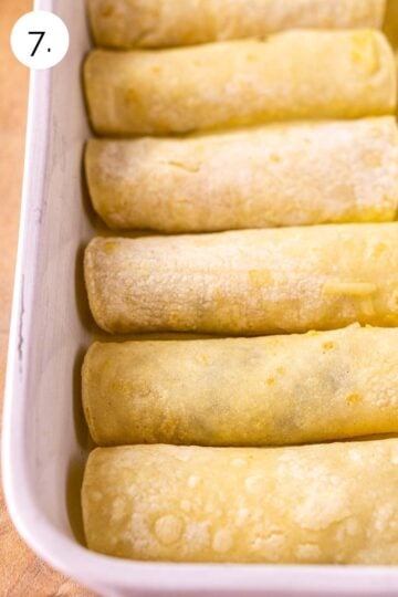 The enchiladas placed in a white baking dish facing seam-side down before topping with the sauce and cheese.