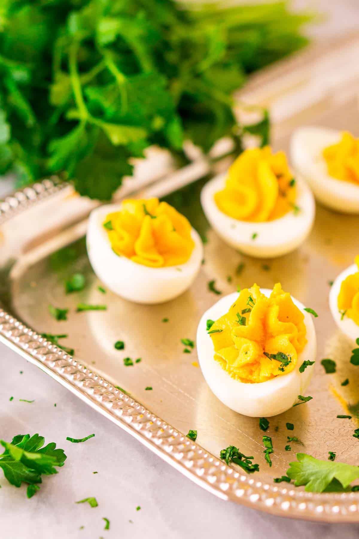 A close-up view of a truffle deviled egg on a silver platter on a white marble countertop with chopped parsley around it.