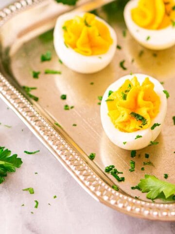 Several truffle deviled eggs on a silver serving platter on a white marble countertop with a bunch of fresh parsley in the background.