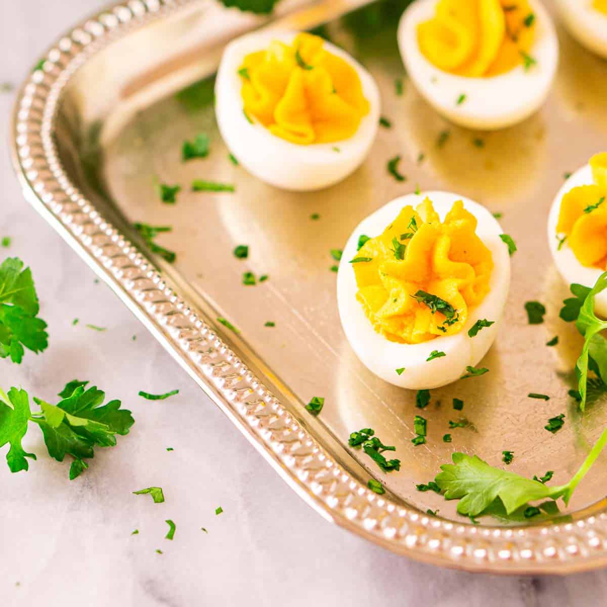 Several truffle deviled eggs on a silver platter with fresh parsley around them.