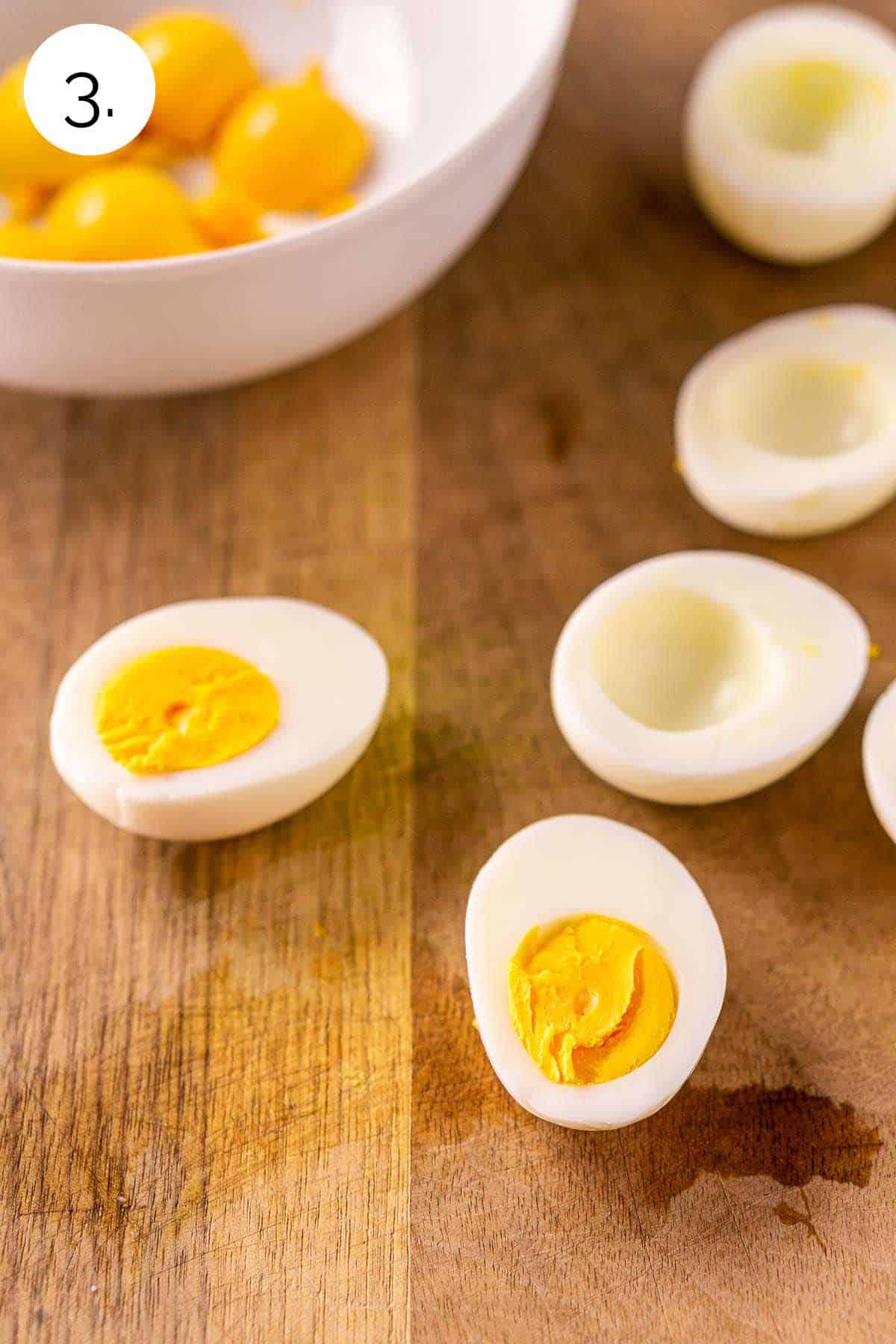 The steamed eggs cut in half on a brown cutting board with some of the egg yolks removed and place in a small white bowl.