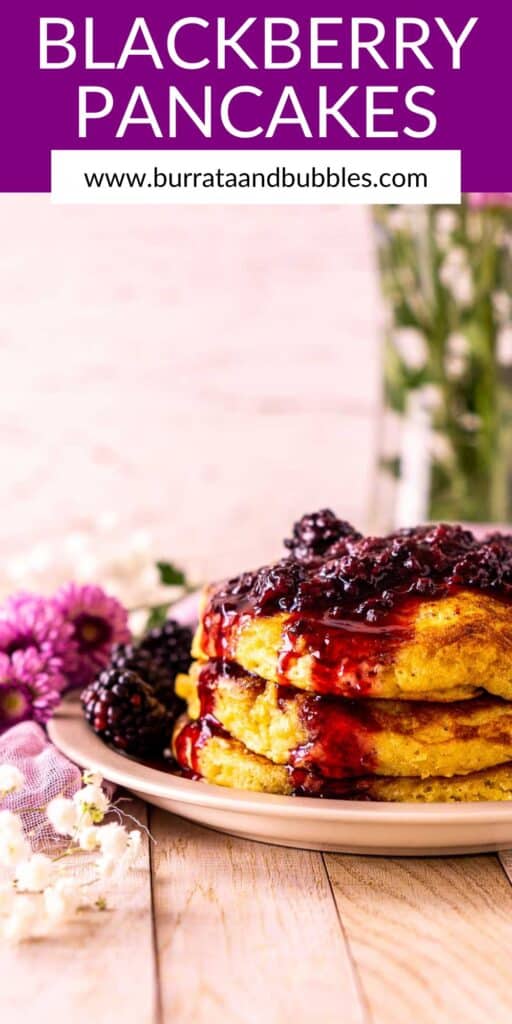 A stack of blackberry pancakes on a small plate with flowers to the left and text overlay on top.