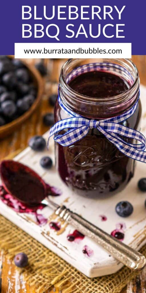A mason jar filled with the blueberry BBQ sauce on a white wooden board with text overlay on top of the image.