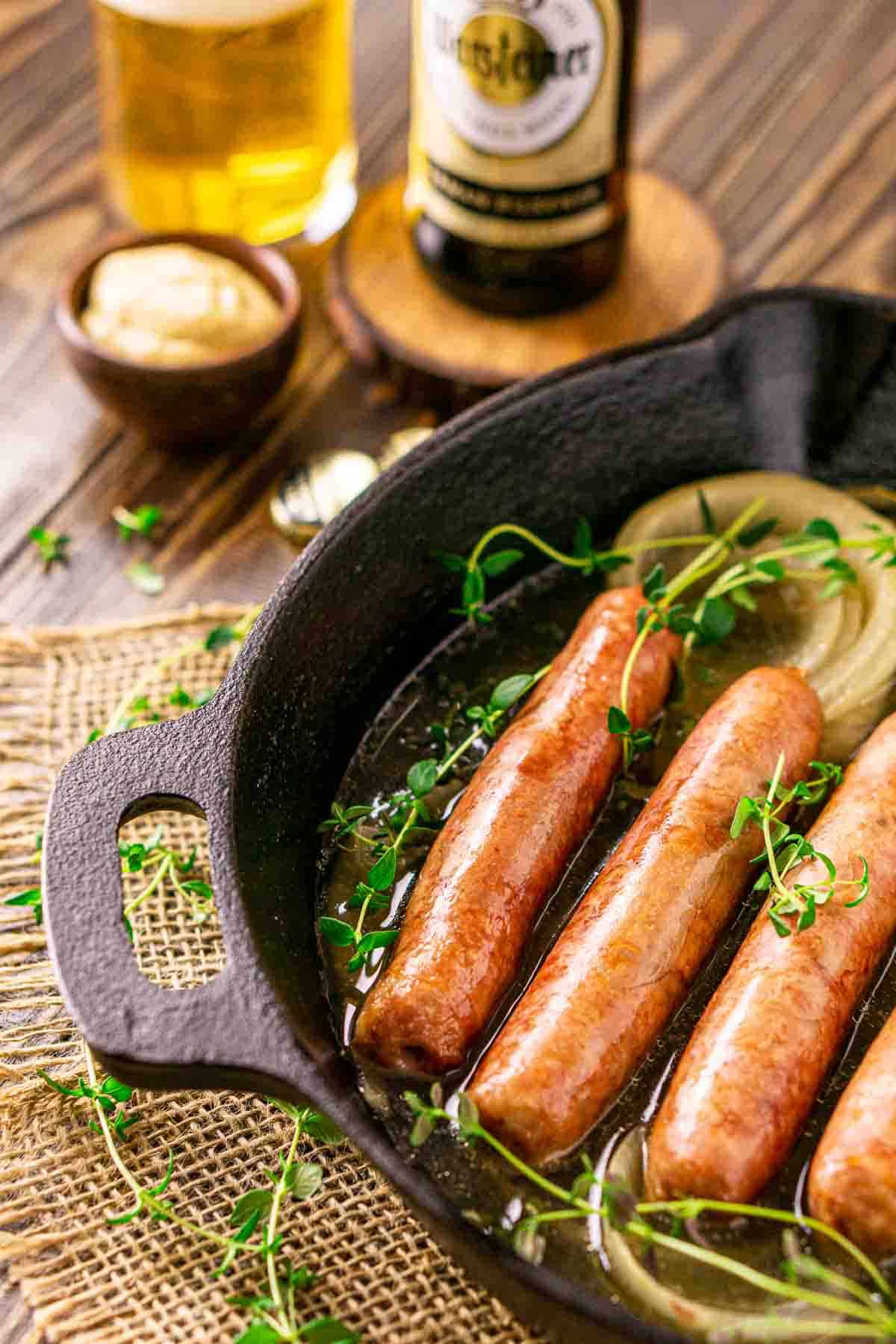 A side view of the cast-iron skillet with the smoked brats on top of burlap and a bottle and glass of beer to the upper left.