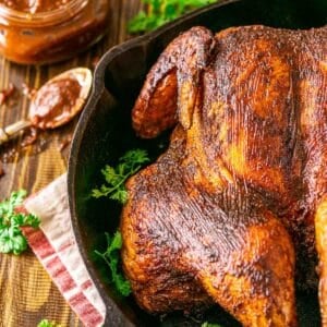 The smoked spatchcock chicken in a black cast-iron skillet on a brown wooden surface with BBQ sauce in the corner.