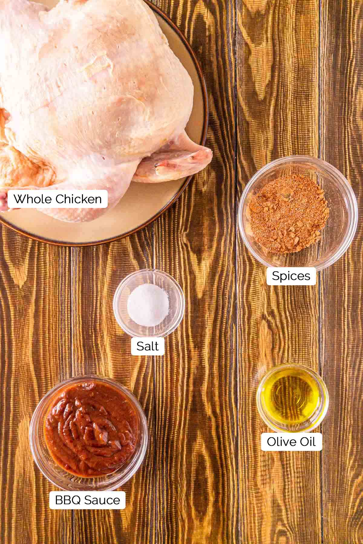 The ingredients for smoking the chicken on a brown wooden surface with black and white labels by the items.