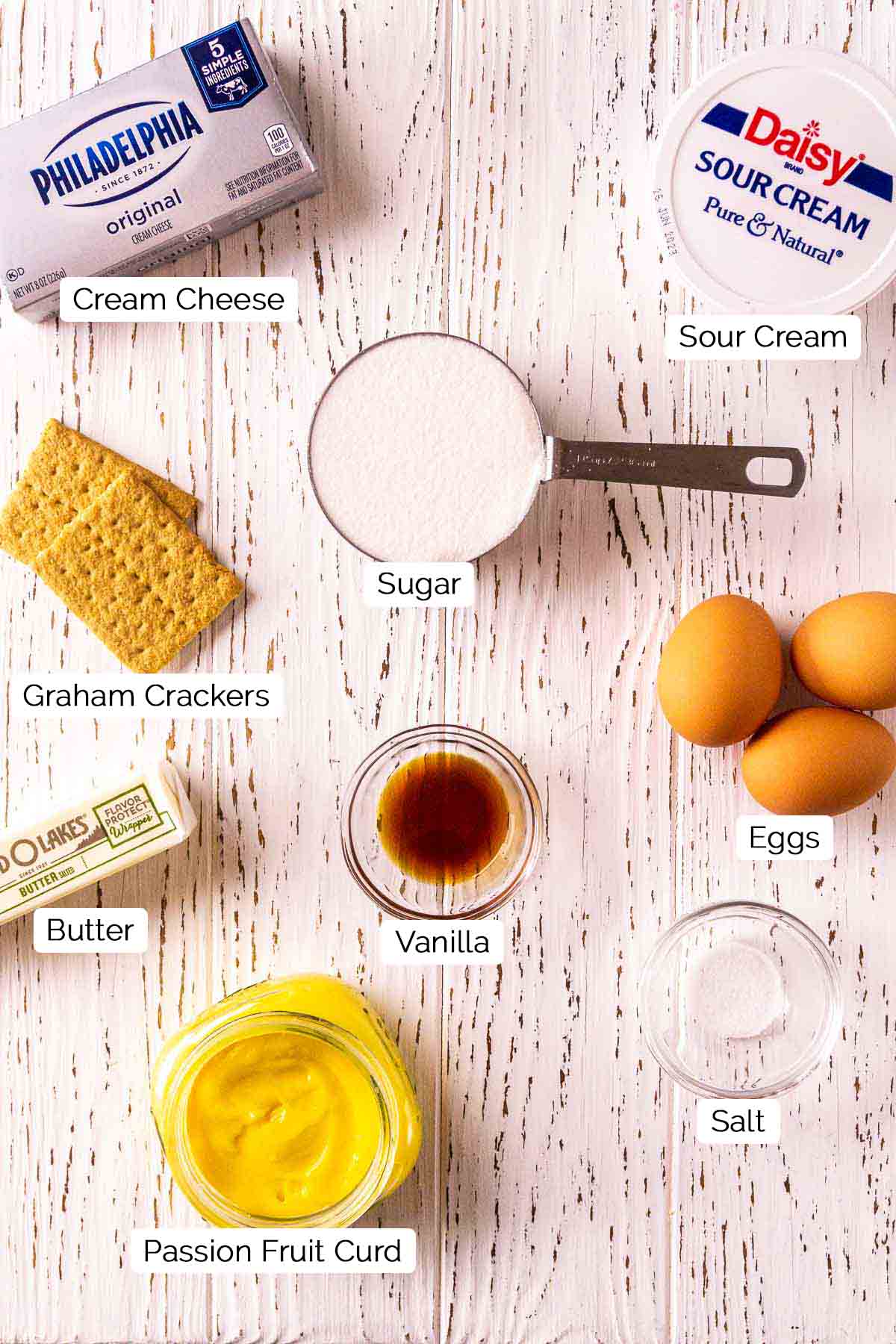 The cheesecake ingredients on a white wooden surface with white and black labels by the items.