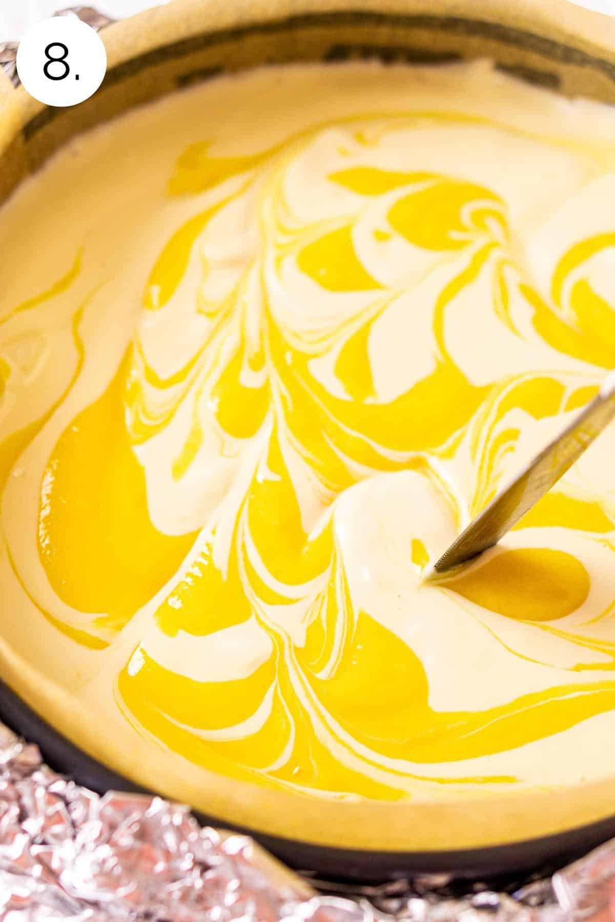 A knife swirling the passion fruit curd in the cheesecake filling in the springform pan before baking.