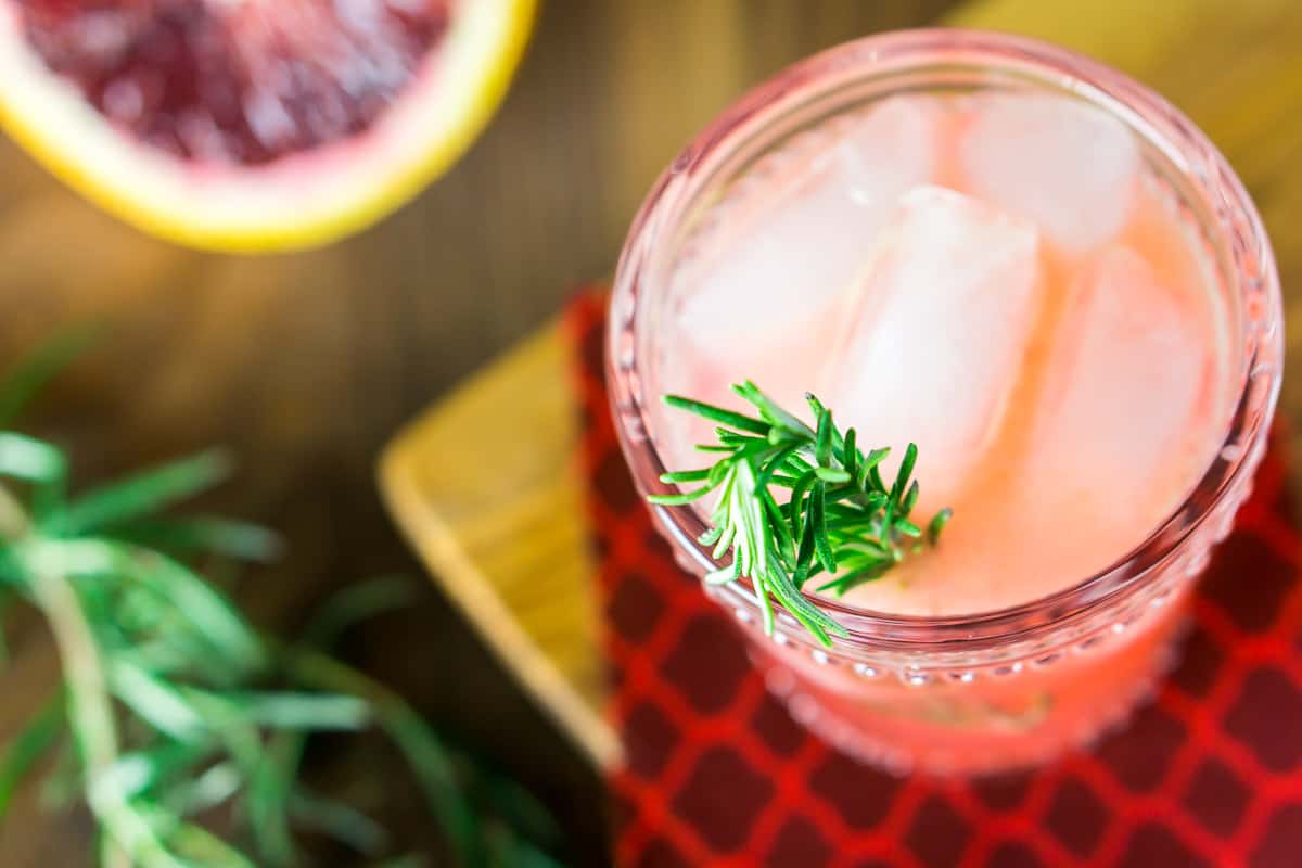 An aerial view of the blood orange gin and tonic on a wooden tray with a fresh rosemary sprig coming out of the glass.