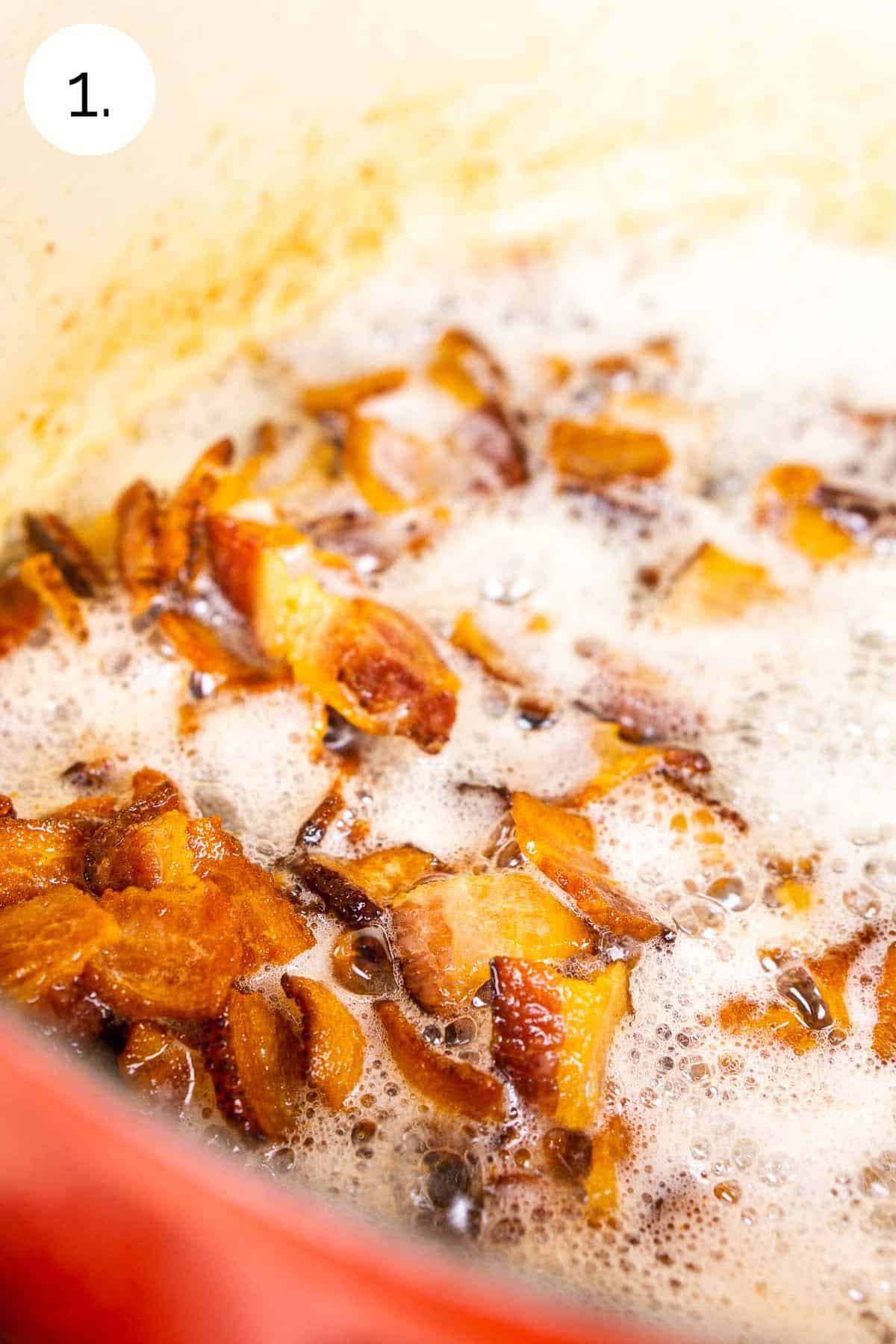 The bacon in a red Dutch oven after it has turned foamy as the fat has rendered out of the meat.