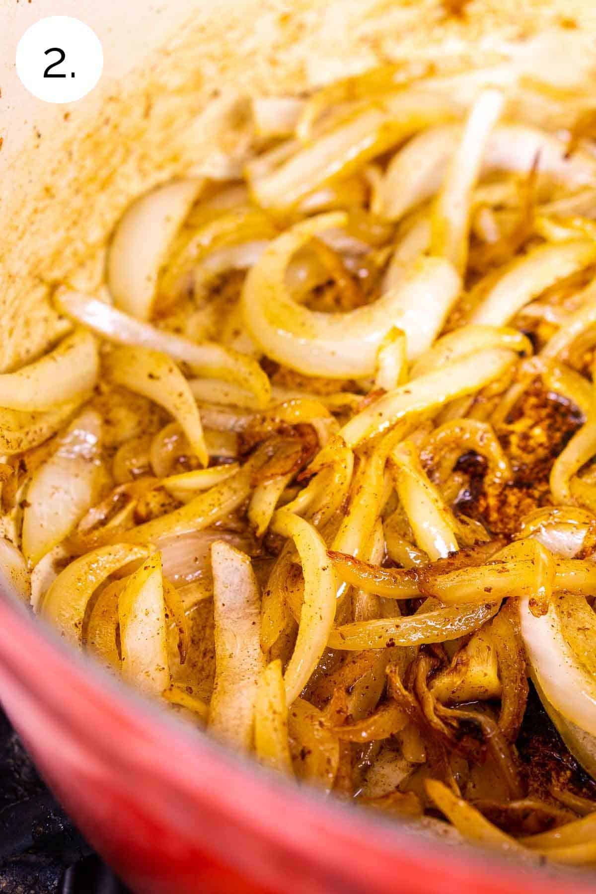 The sliced onions caramelizing in leftover bacon fat in a red Dutch oven on the stove-top range.