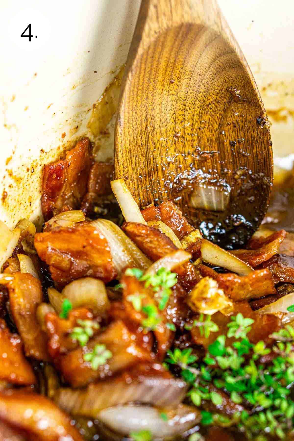 A wooden spoon stirring in the bourbon and thyme with the rest of the ingredients in a red Dutch oven on the stove.