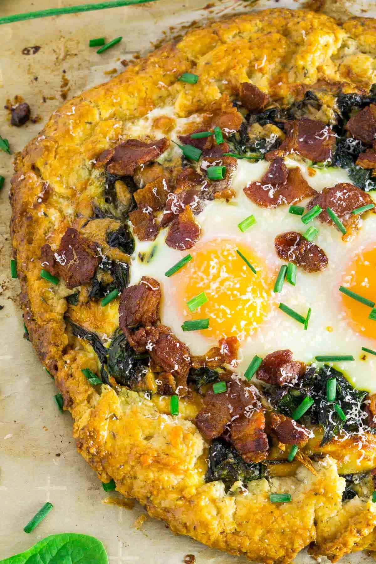 An aerial view of the breakfast galette on a piece of brown parchment paper with spinach and chives to the side.