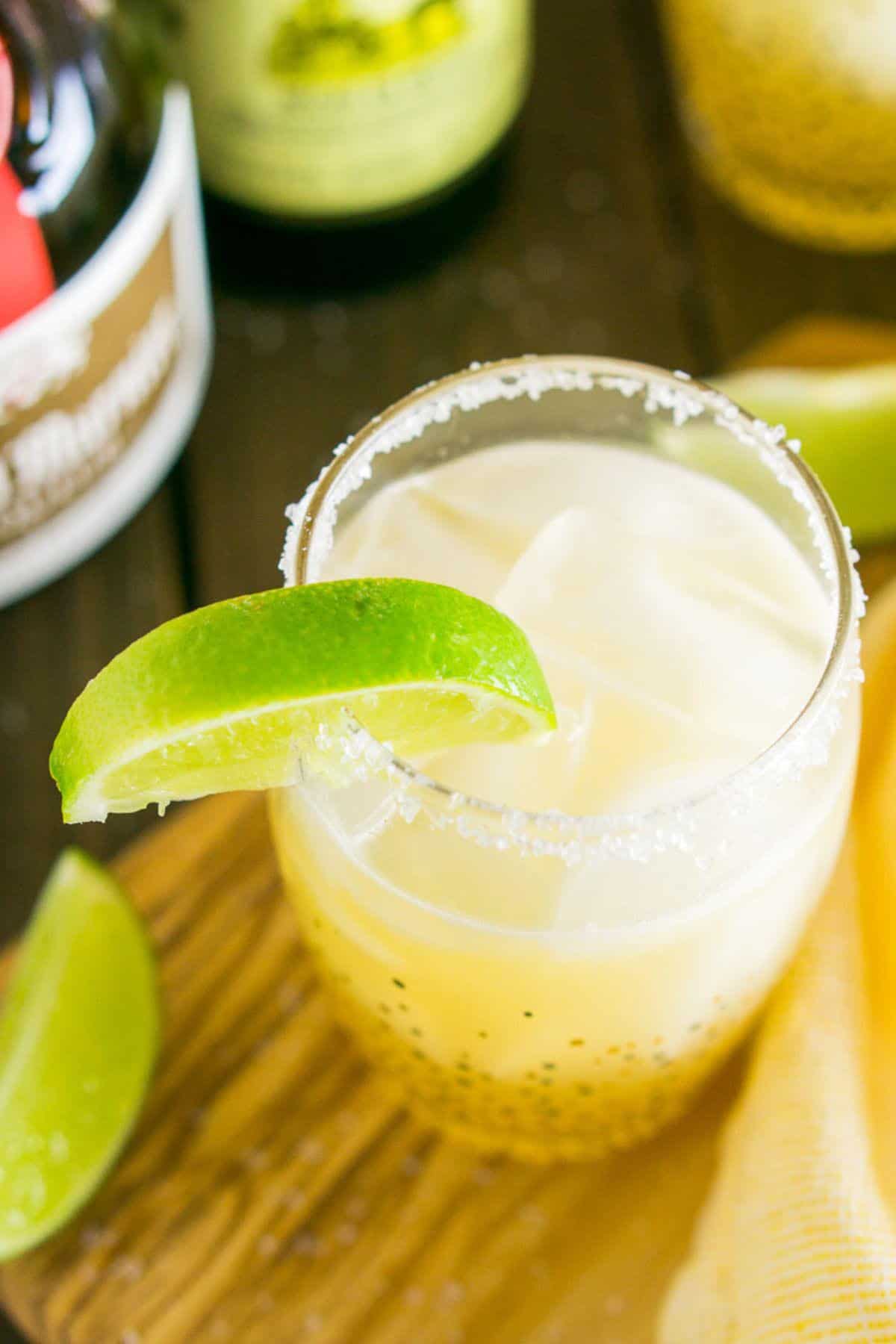 An aerial view of the classic margarita on a wooden serving tray with a yellow napkin and lime slice on the side.