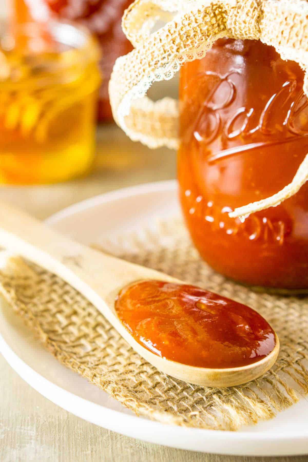 A close-up shot of a wooden spoon filled with the honey-sriracha BBQ sauce on a piece on burlap set on top of a small white plate.