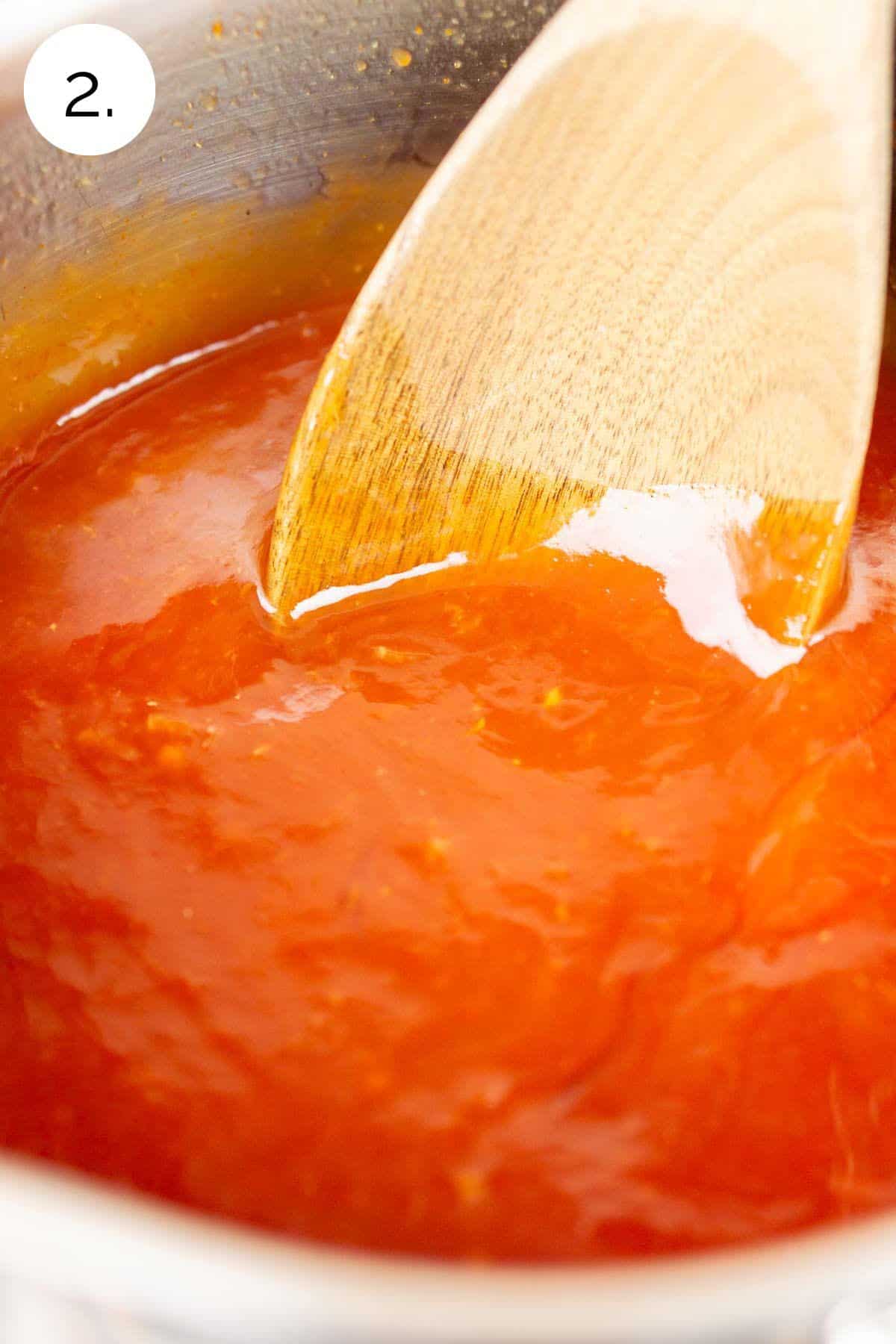 A wooden spoon stirring the sauce in a small stainless steel saucepan on the stove-top range to combine the ingredients.
