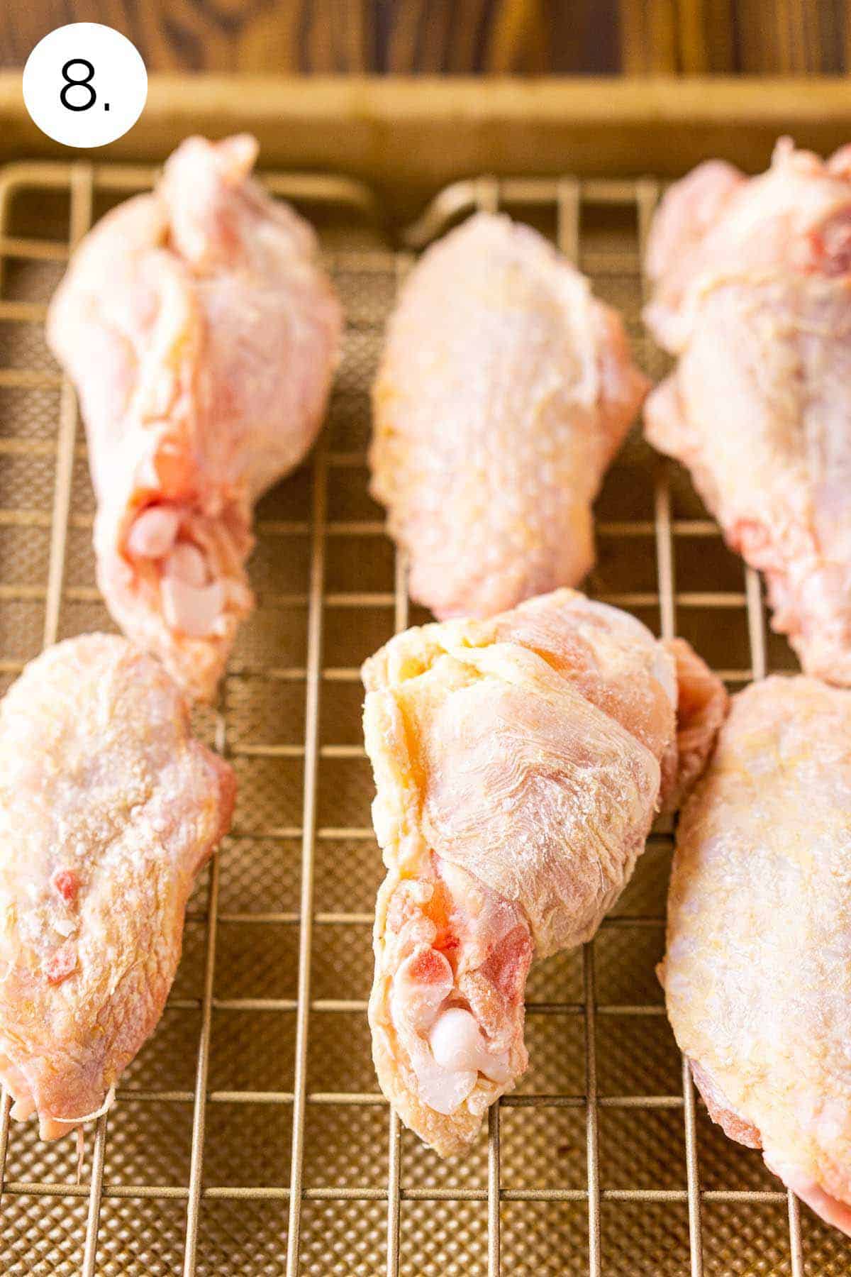 The wings on a gold wire rack on top of a baking sheet after they're tossed with baking powder and before they bake in the oven.