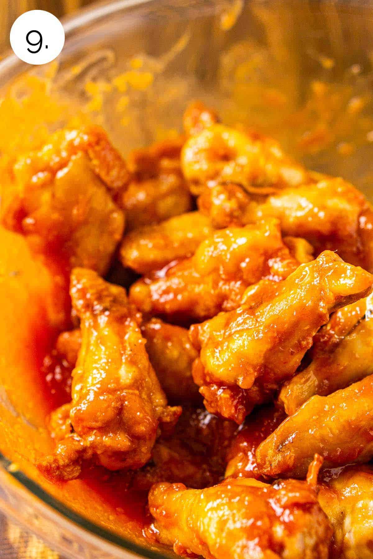 The wings in a large glass mixing bowl after they've been tossed with the homemade honey-sriracha BBQ sauce.
