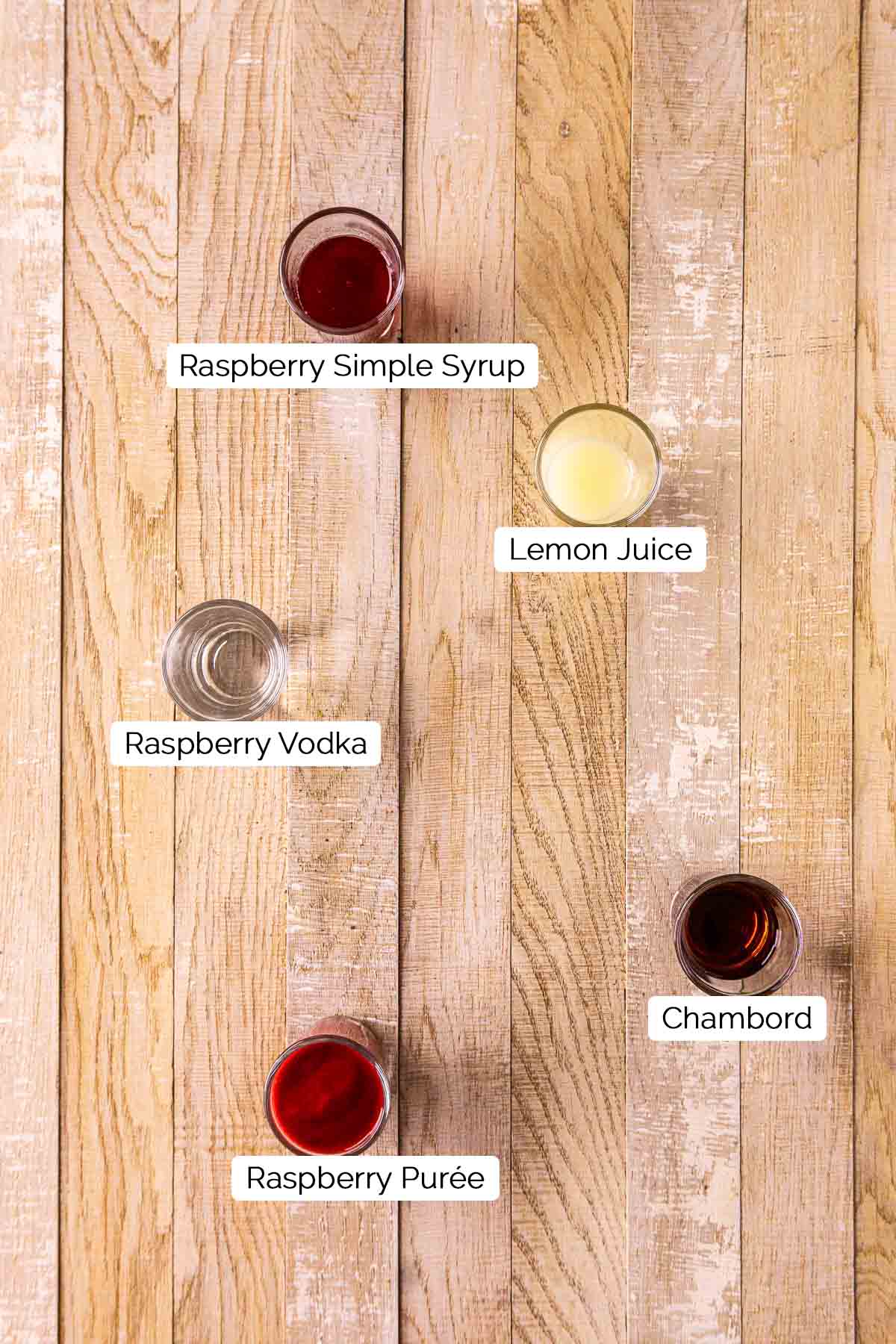 The drink ingredients with black and white labels on a cream-colored wooden board.