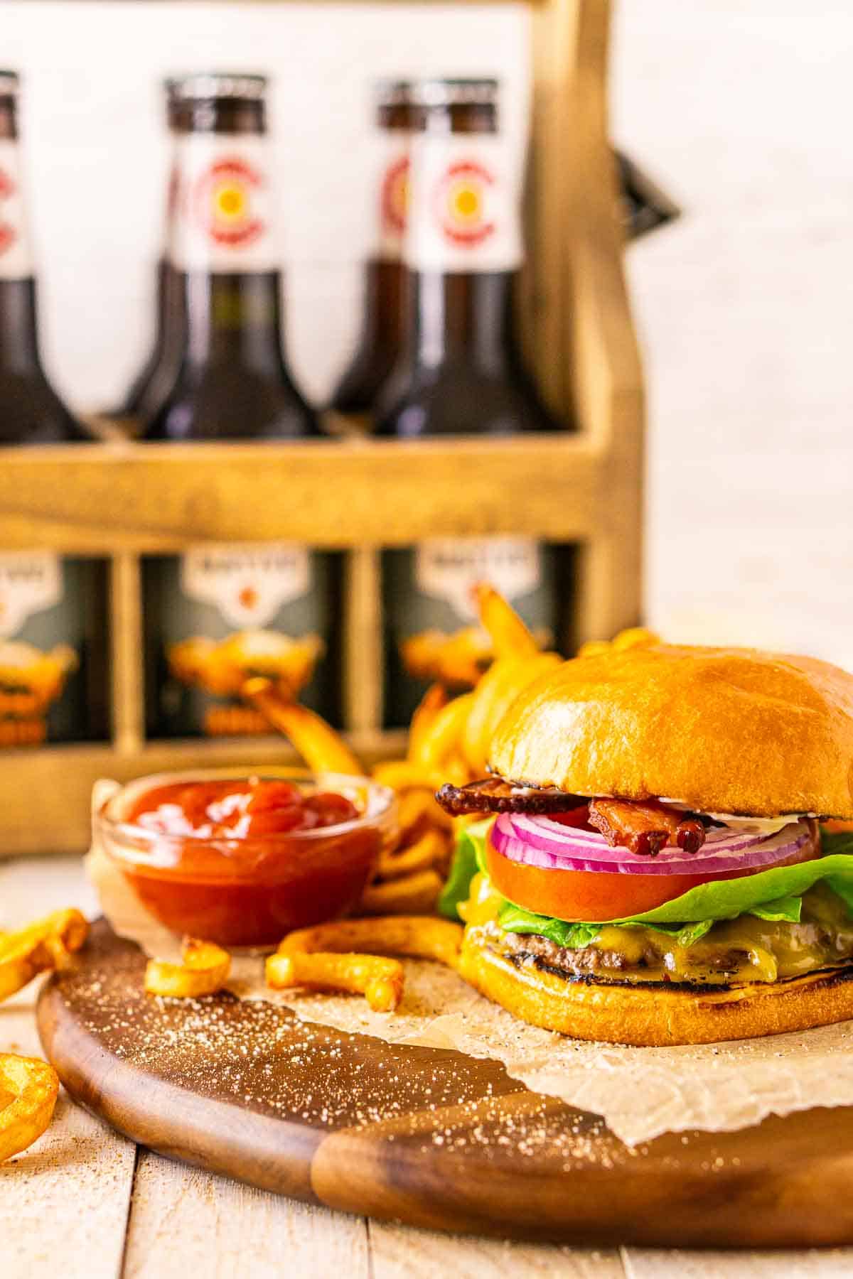 The Wagyu burgers on a wooden plate with parchment paper and a six pack of beer in the background.