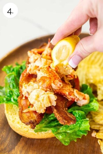 A hand squeezing fresh lemon juice on top of the lobster before putting the top bun on the meat.