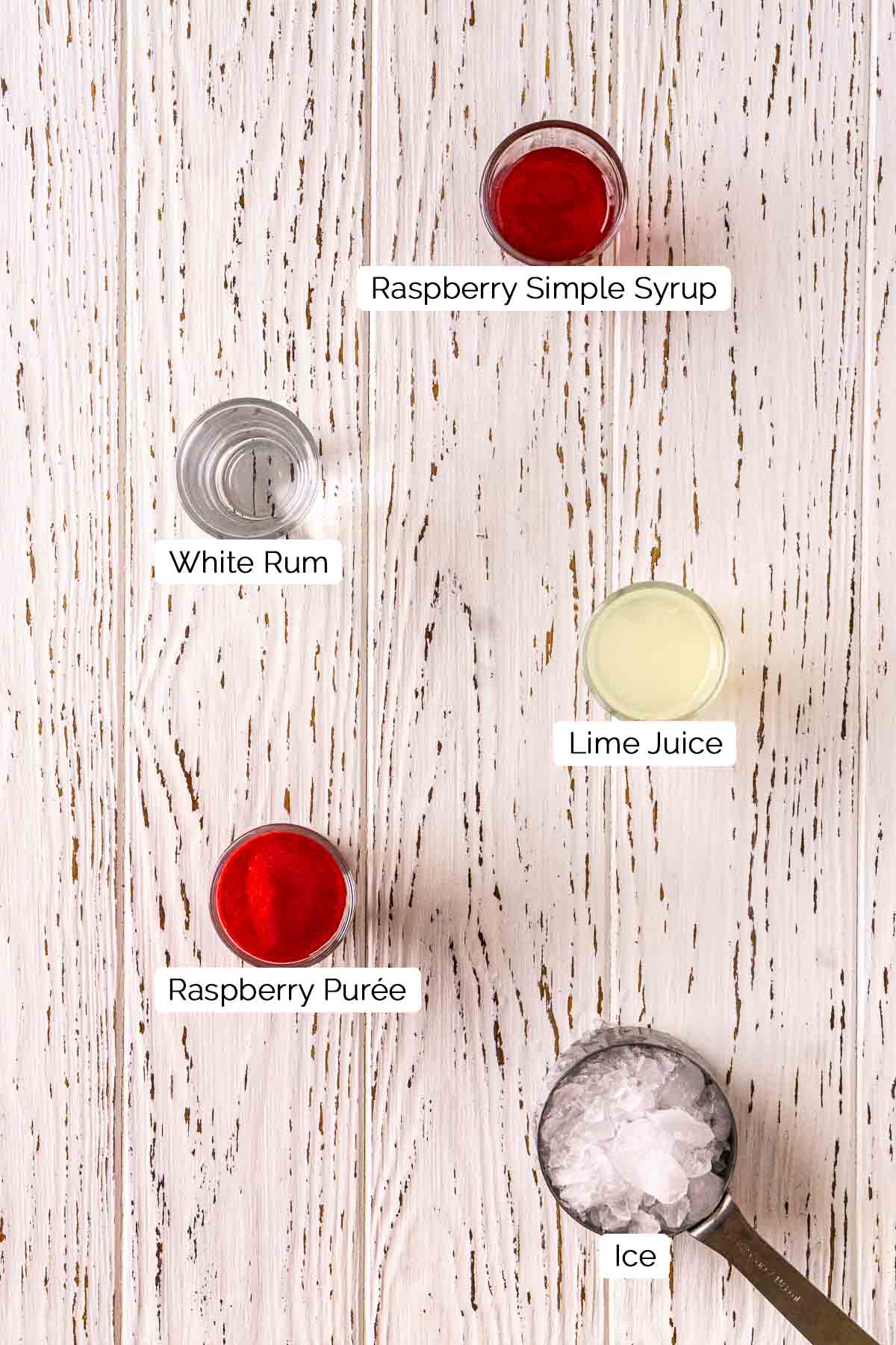 The drink ingredients with white and black labels by the items on a white distressed wooden board.